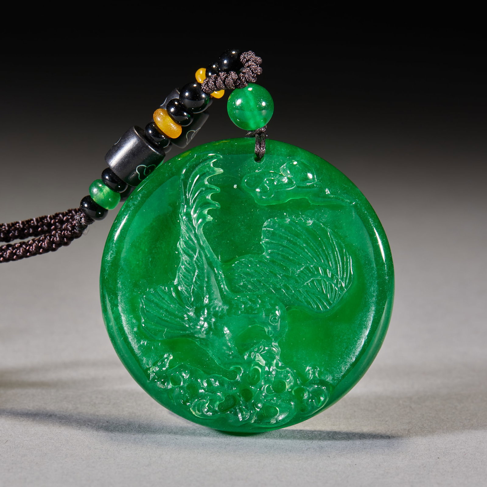 Jadeite Eagle Plaque: A jadeite plaque carved as an eagle, bold head, wings spread to fly, symbolising far-seeing vision. Green and warm, finely carved, with a hole at the top ?? a pendant. Diameter 5.1 cm, T 1.2 cm, 62 g.