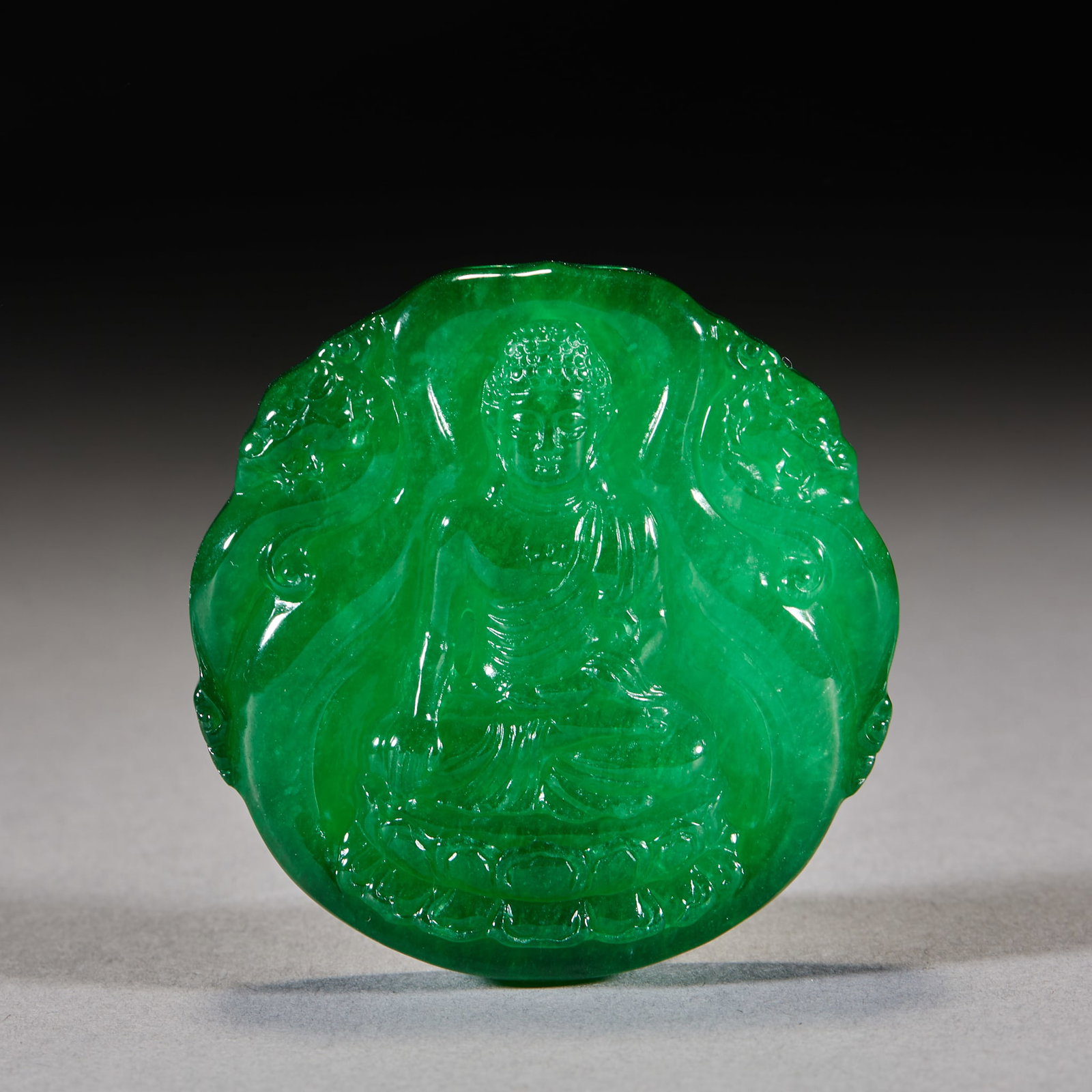 Jadeite Sakyamuni Plaque: A jadeite plaque carved with Sakyamuni in lotus position, solemn face. Green and warm, finely carved ?? an amulet Buddhist plaque for wearing. Diameter 5.4 cm, T 1.2 cm, 76 g.
