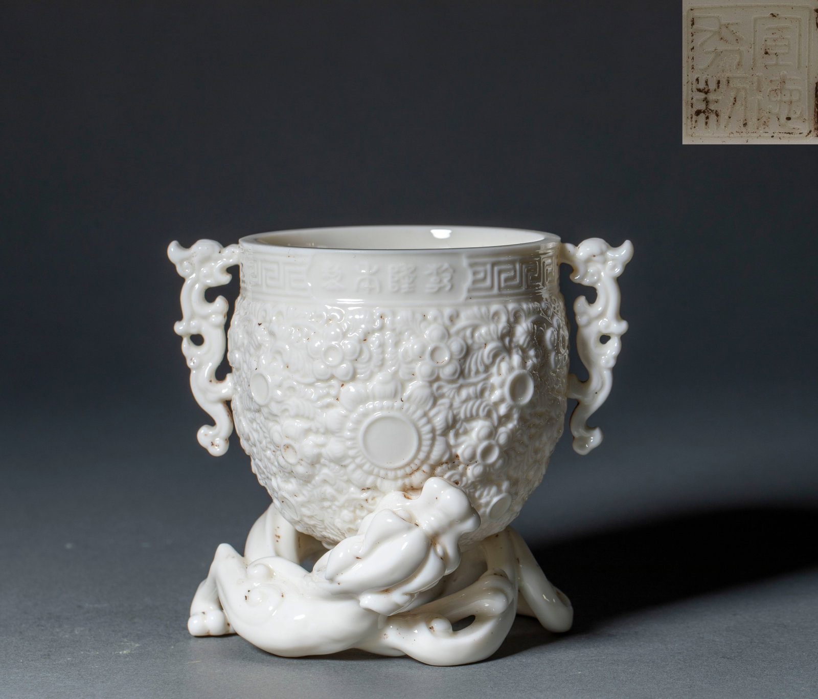 He Chaozong Dehua Kiln Chi-Dragon Floral Cup: A He Chaozong Dehua white-porcelain cup carved with a chi-dragon and floral decoration, warm white glaze. He Chaozong was a celebrated Ming Dehua kiln porcelain sculptor; this cup carries his style.