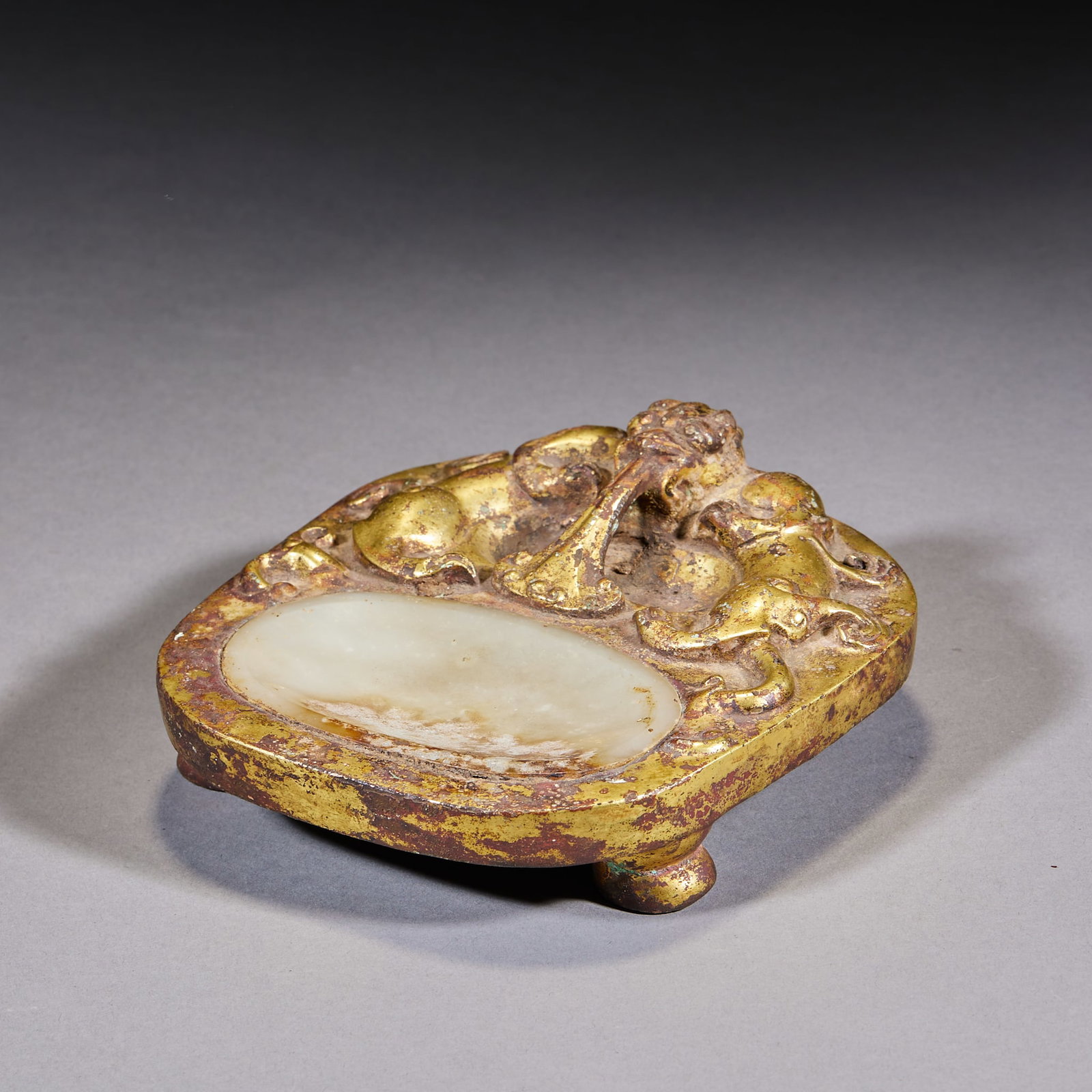 Gilt Copper Jade-Inlaid Dragon-Drinking-Water Tripod Inkstone: An inkstone of gilt copper inlaid with jade, carved with a dragon-drinking-water motif, on three feet. Bright gilding and warm jade ?? a major scholar's inkstone. H 6 cm, L 15 cm, W 13.5 cm.