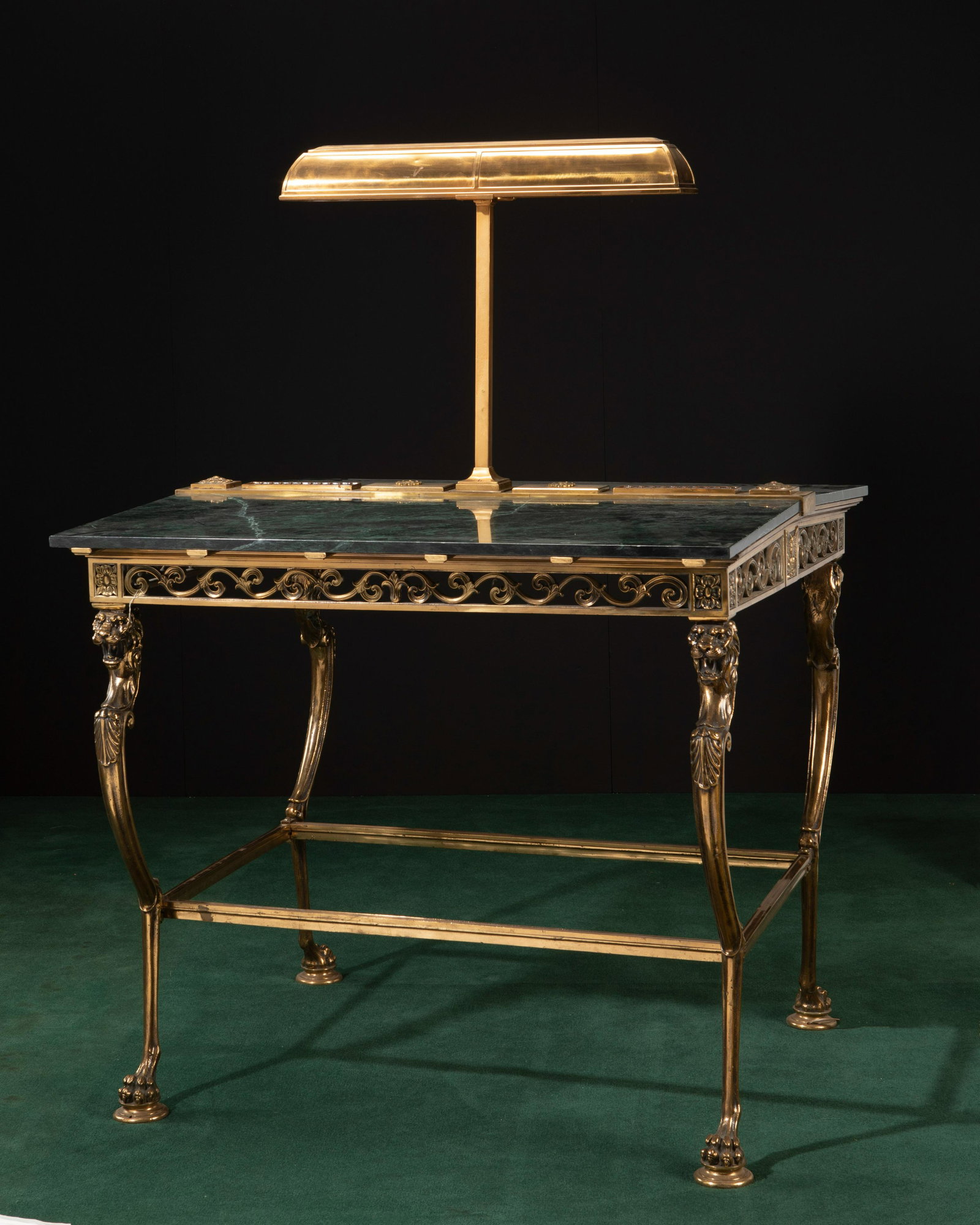 A bronze banker's table: A bronze banker's table Early 20th century With dark green marble canted top centering a lighted platform on bronze base with reticulated vine details over lion head supports and paw feet with lower s