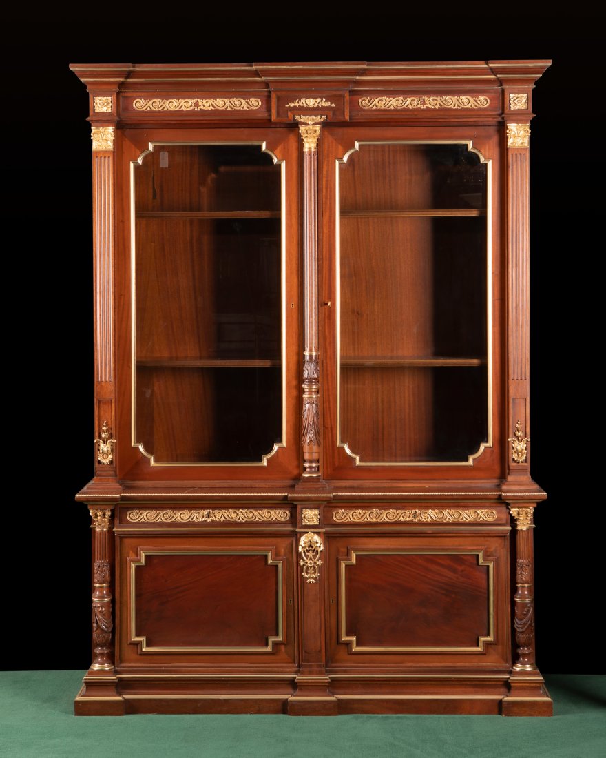 A Continental biblioteque: A Continental biblioteque Early 20th century In carved mahogany with applied gilt-bronze mounts, the molded and stepped pediment over glazed double doors with two interior shelves over two drawers and