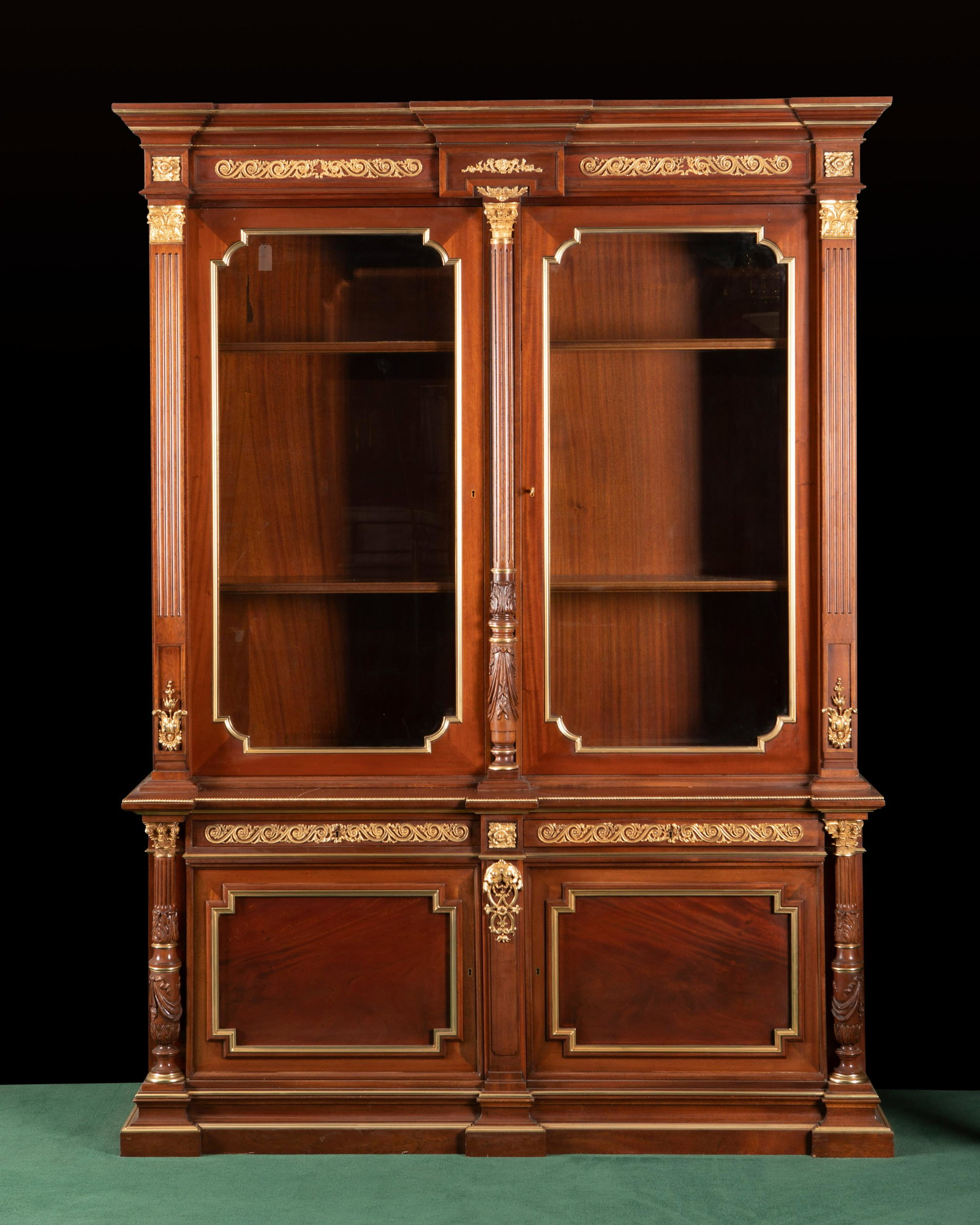 A Continental biblioteque: A Continental biblioteque Early 20th century In carved mahogany with applied gilt-bronze mounts, the molded and stepped pediment over glazed double doors with two interior shelves over two drawers and