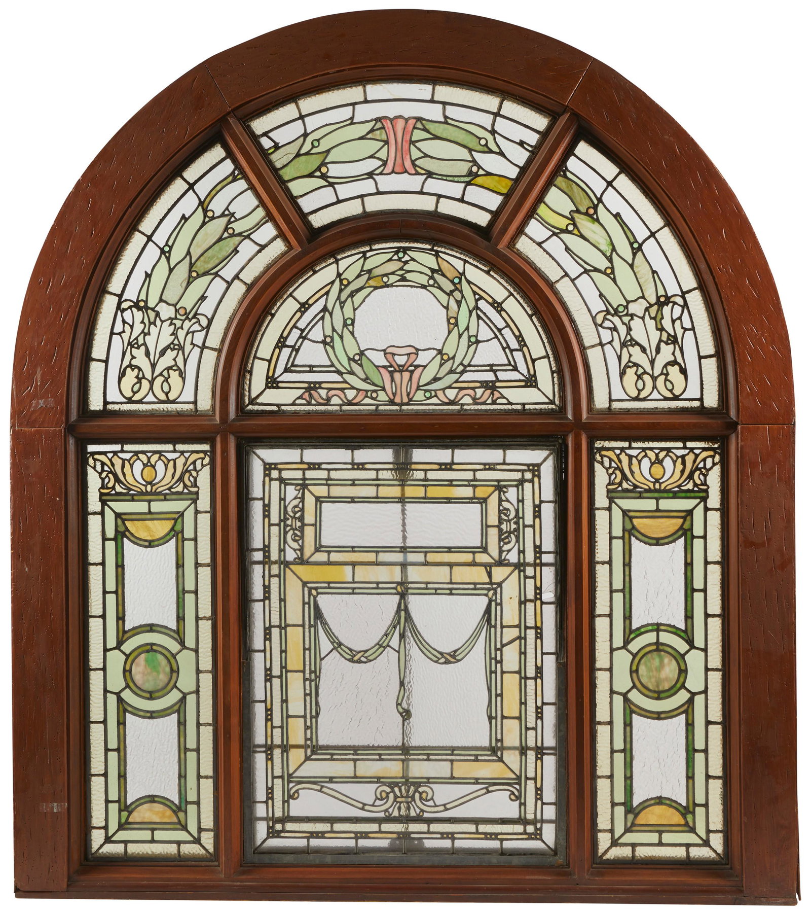 A leaded arched glass window: A leaded arched glass window Early 20th century/American 7 panels of multicolored glass of amber pinks and greens with paneled and side panels surrounding a central wreath design Sight: 67" H x 5