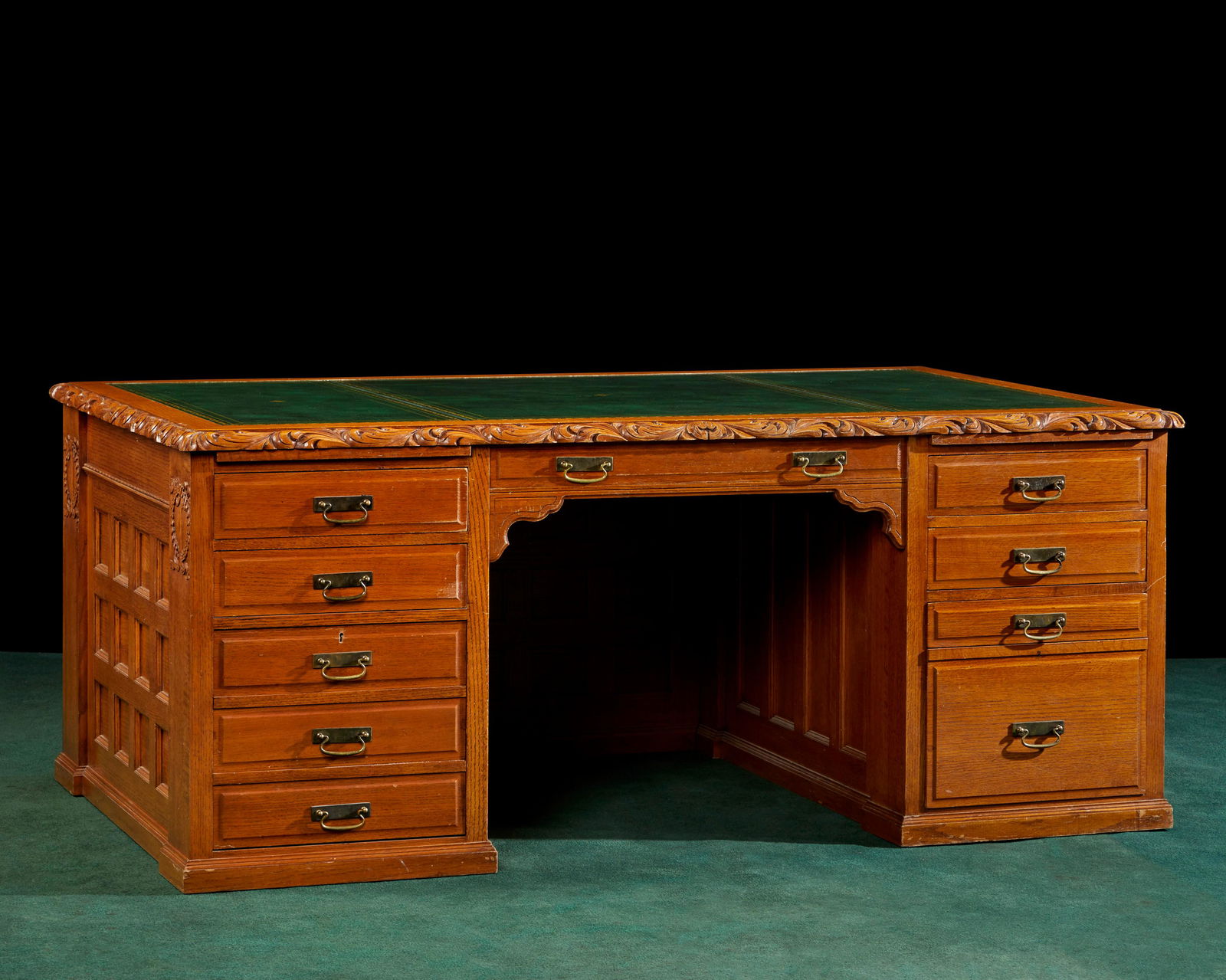 A carved oak executive desk with brass hardware: A carved oak executive desk with brass hardwareEarly 20th centuryWith new inset green leather top under glass with coffered paneling and two stacks of five drawers30.5" H x 71.5" W x 42"