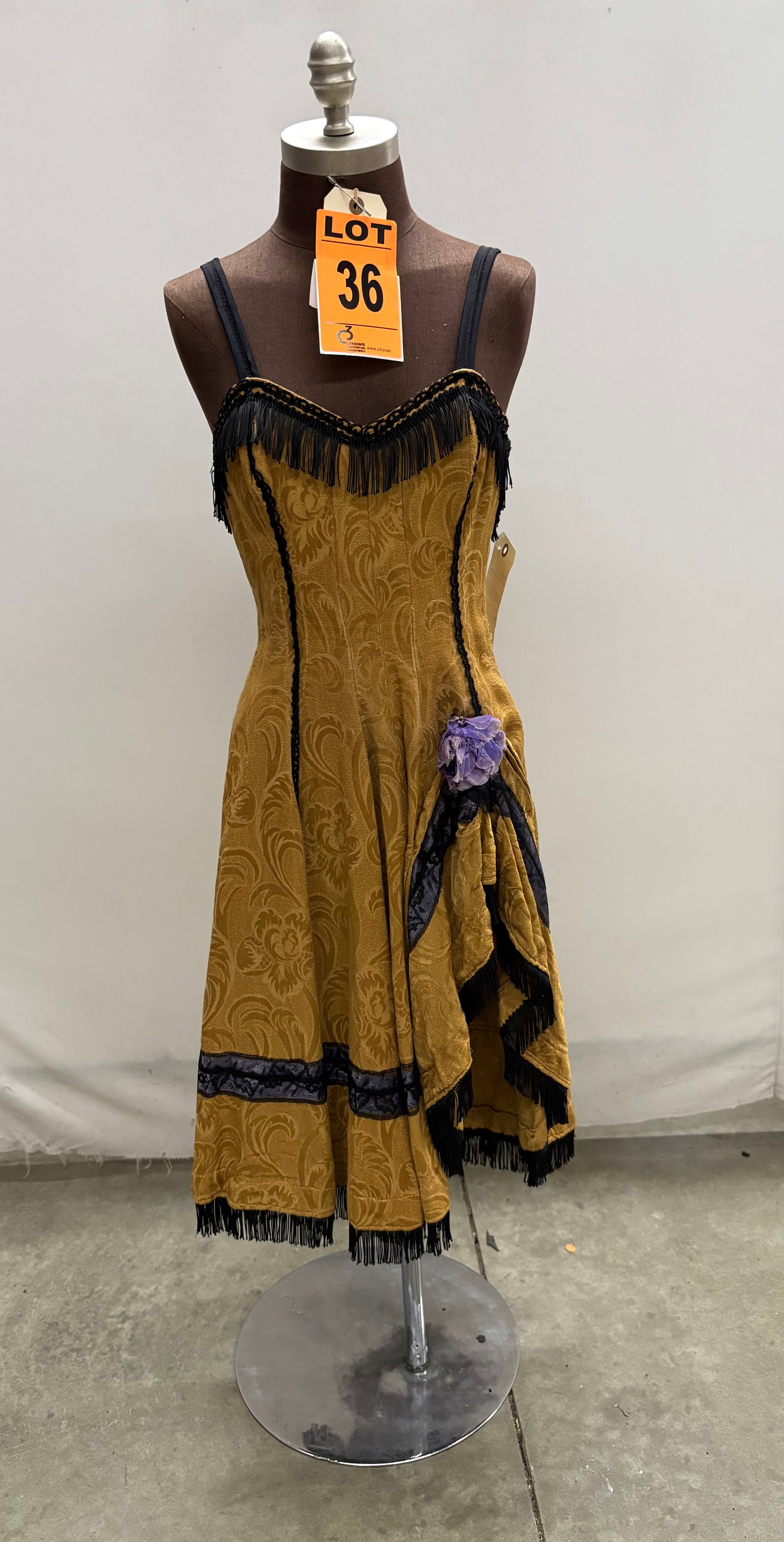 Saloon girl costume, n/a, gold brocade, black fringe with purple flower, studio made.: Saloon girl costume, n/a, gold brocade, black fringe with purple flower, studio made. IMPORTANT NOTE TO BIDDERS: We are not an auction gallery but a liquidator retained by CRC as they wind-down operat