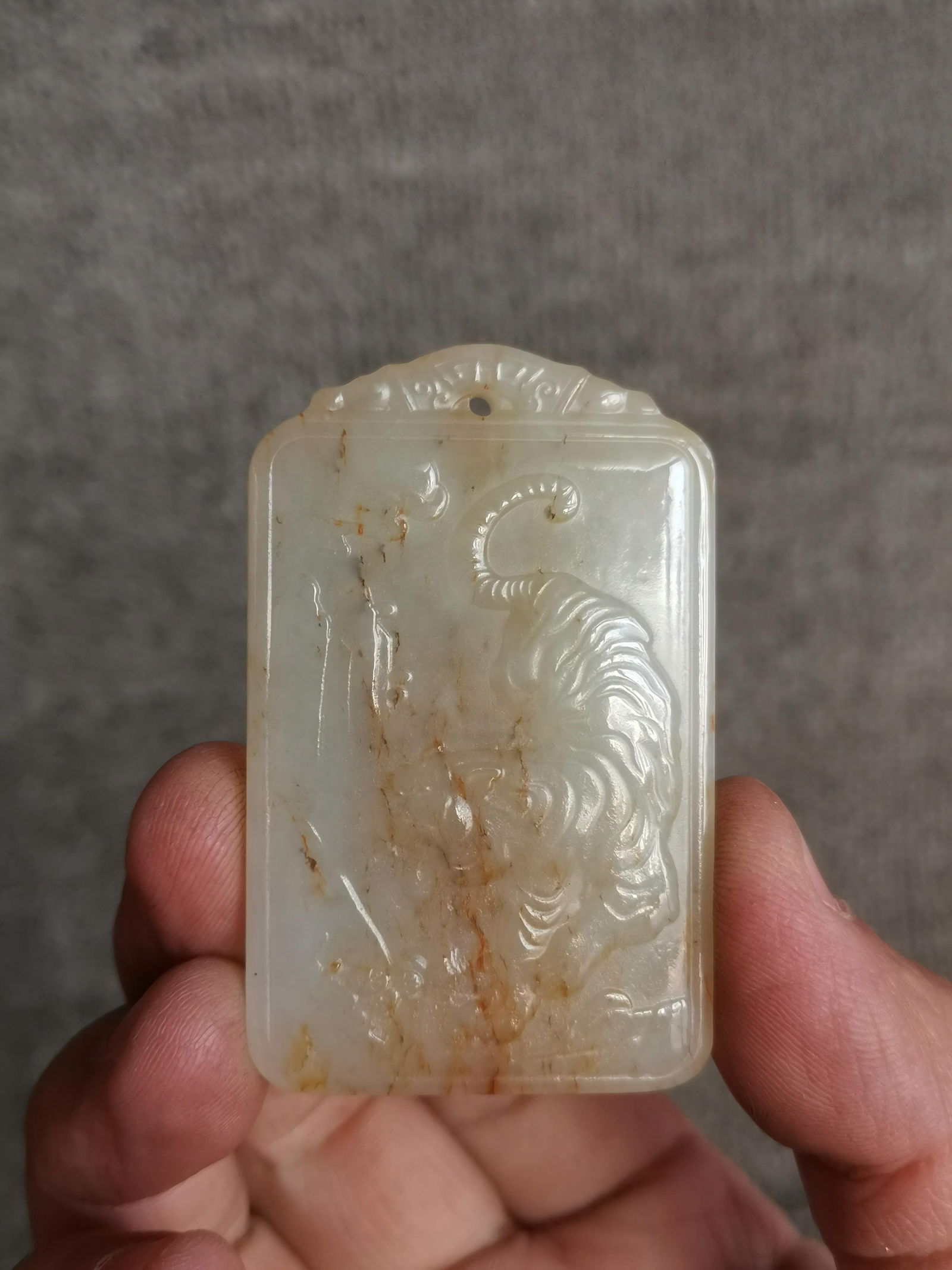 Qing Dynasty Hetian jade carving of a tiger descending a mountain: This Qing Dynasty Hetian jade pendant, carved with a tiger descending a mountain, is made of warm, lustrous Hetian white jade, with natural golden-brown inclusions in some areas. The pendant features