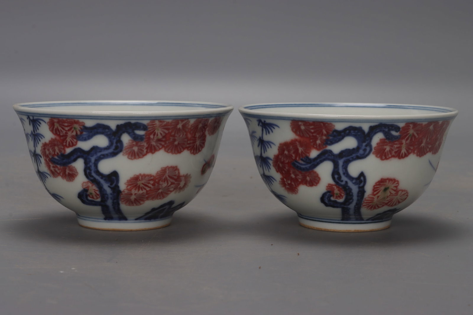 A pair of Ming Dynasty Xuande blue and white underglaze red pine, bamboo and plum cups: A pair of blue-and-white underglaze red pine, bamboo, and plum blossom cups from the Xuande period of the Ming Dynasty, each measuring 4.5 cm in height, 8.5 cm in diameter at the mouth, and 4 cm in di