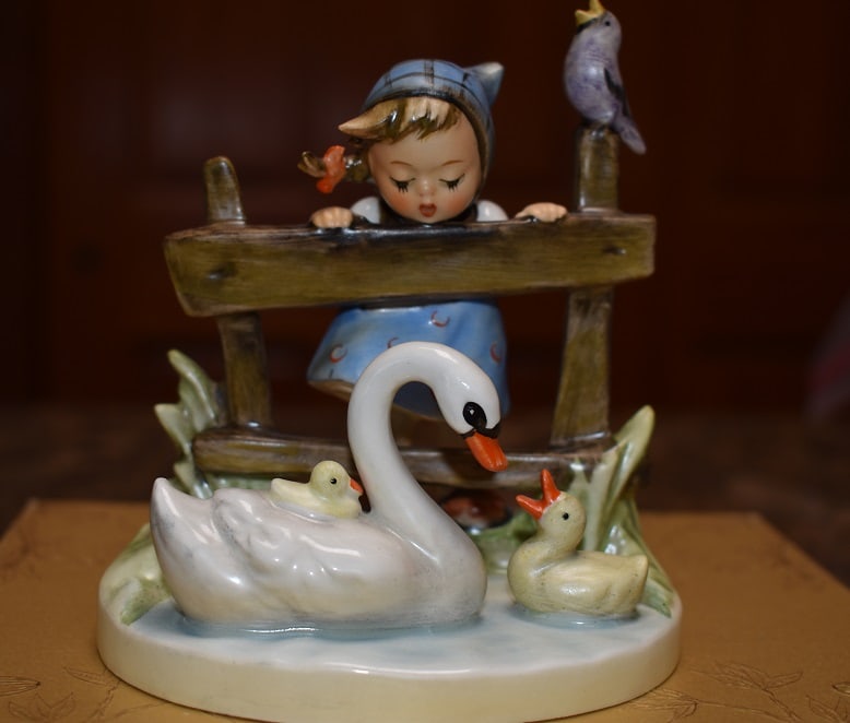 Hummel- Feathered Friends Figurine: Hummel 4 1/2" High by 4" "Feathered Friends" titled Figurine, depicts a really cute girl looking over a fence at her swan with it's 2 babies. No issues, incsed 1956, 344 and 48 on bottom, mark is Goeb