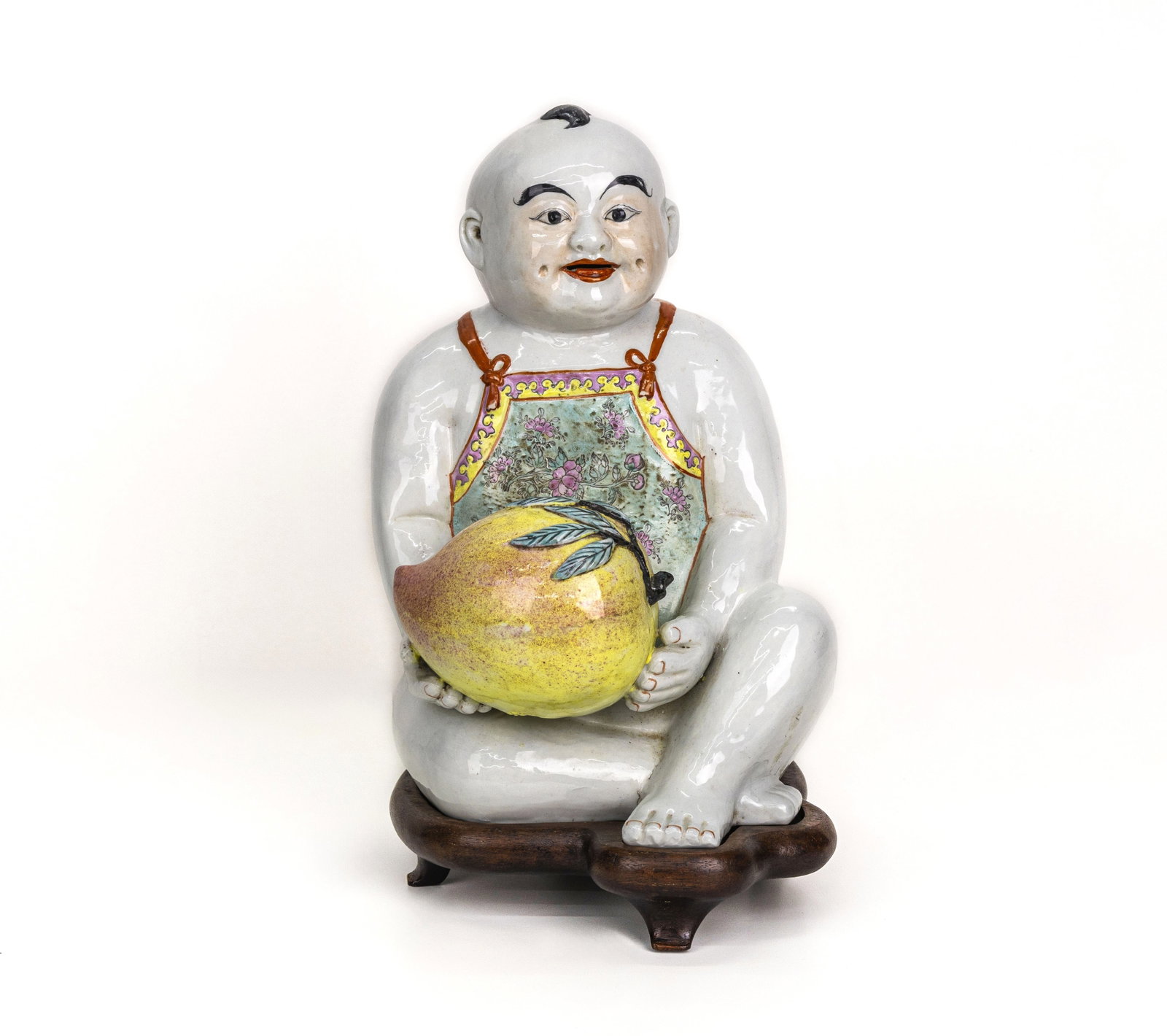 Chinese Porcelain Figure of a Boy Holding Peach: Title: Chinese Polychrome Glazed Porcelain Figure of a Boy Holding a Peach Origin: China Medium: Polychrome glazed porcelain with wood stand Dimensions: 15 ? 9 ?