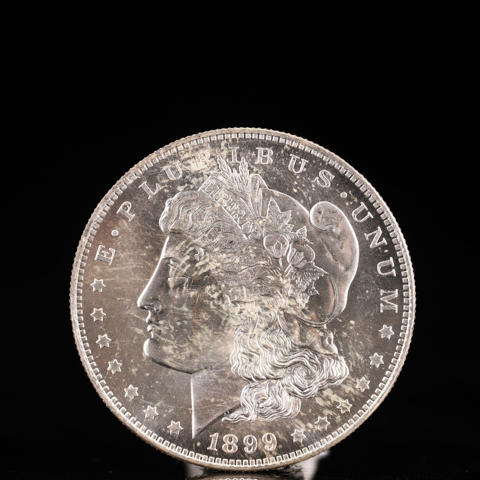 USA Morgan Dollar 1899 Coin: Obv: profile bust with date below and E PLURIBUS UNUM legend and stars around. Rev: eagle with In God we trust above within wreath with UNITED STATES OF AMERICA ONE DOLLAR legend. IN GOD WE TRUST / LI