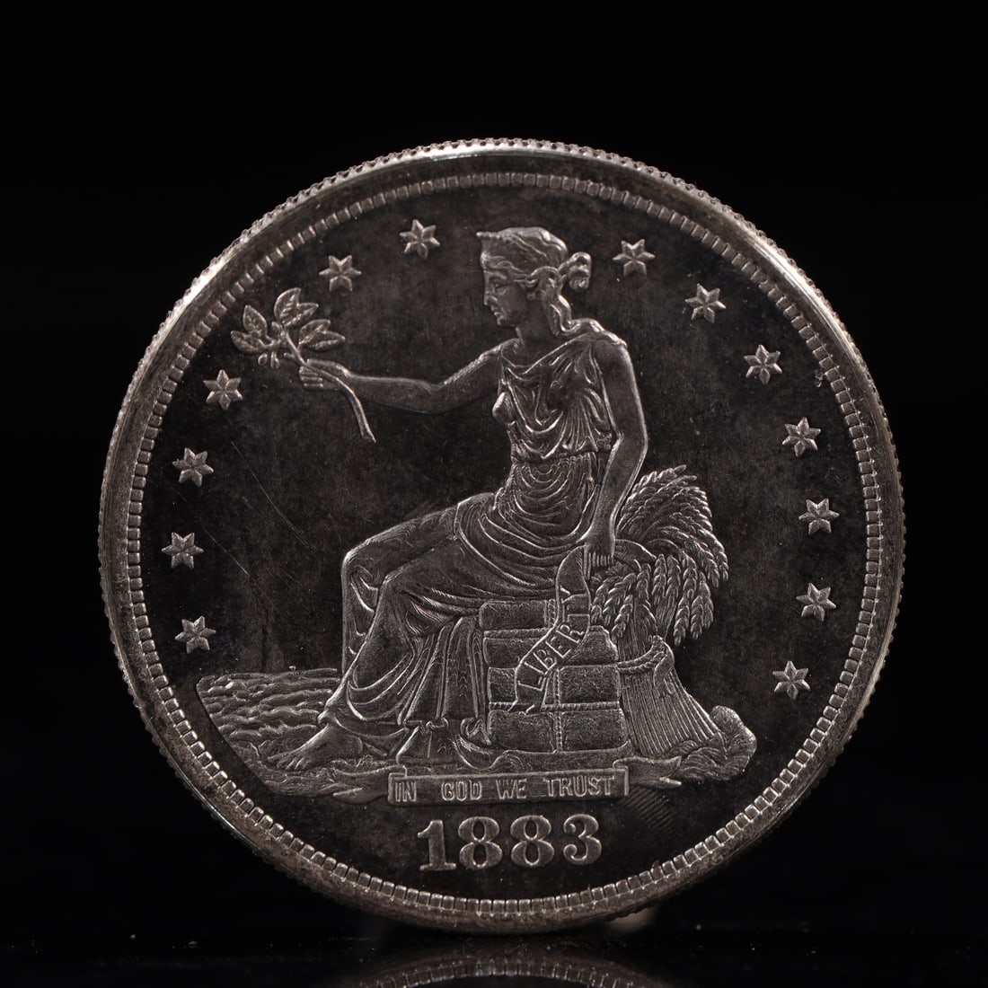 USA Trade Dollar 1883 Coin: American coin. Obverse: Liberty seated on a pedestal facing the sea to the left holding olive branches surrounded by 13 stars. IN GOD WE TRUST / LIBERTY / 1883. Reverse: An eagle holding branches with