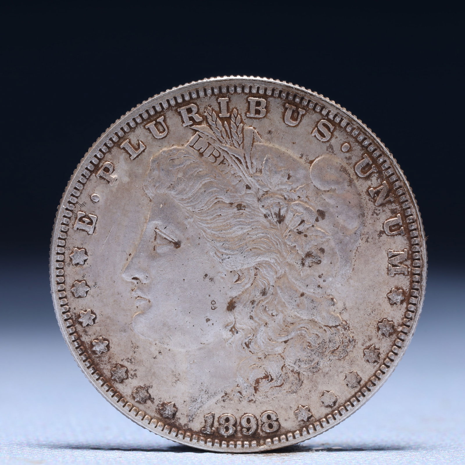 USA Morgan Dollar 1898 Coin: Obv: profile bust with date below and E PLURIBUS UNUM legend and stars around. Rev: eagle with In God we trust above within wreath with UNITED STATES OF AMERICA ONE DOLLAR legend. IN GOD WE TRUST / LI