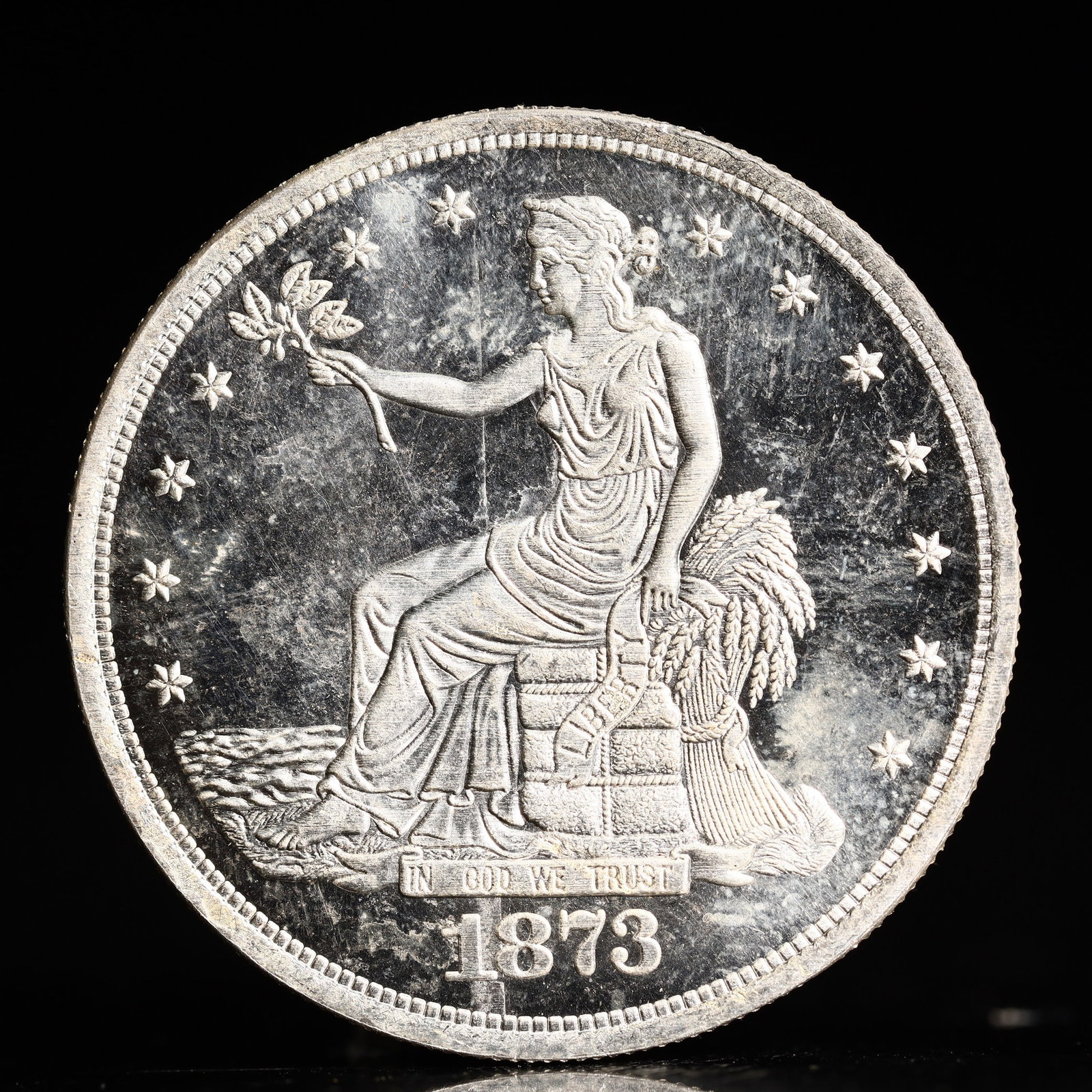 USA Trade Dollar 1873 Coin: American coin. Obverse: Liberty seated on a pedestal facing the sea to the left holding olive branches surrounded by 13 stars. IN GOD WE TRUST / LIBERTY / 1873. Reverse: An eagle holding branches with