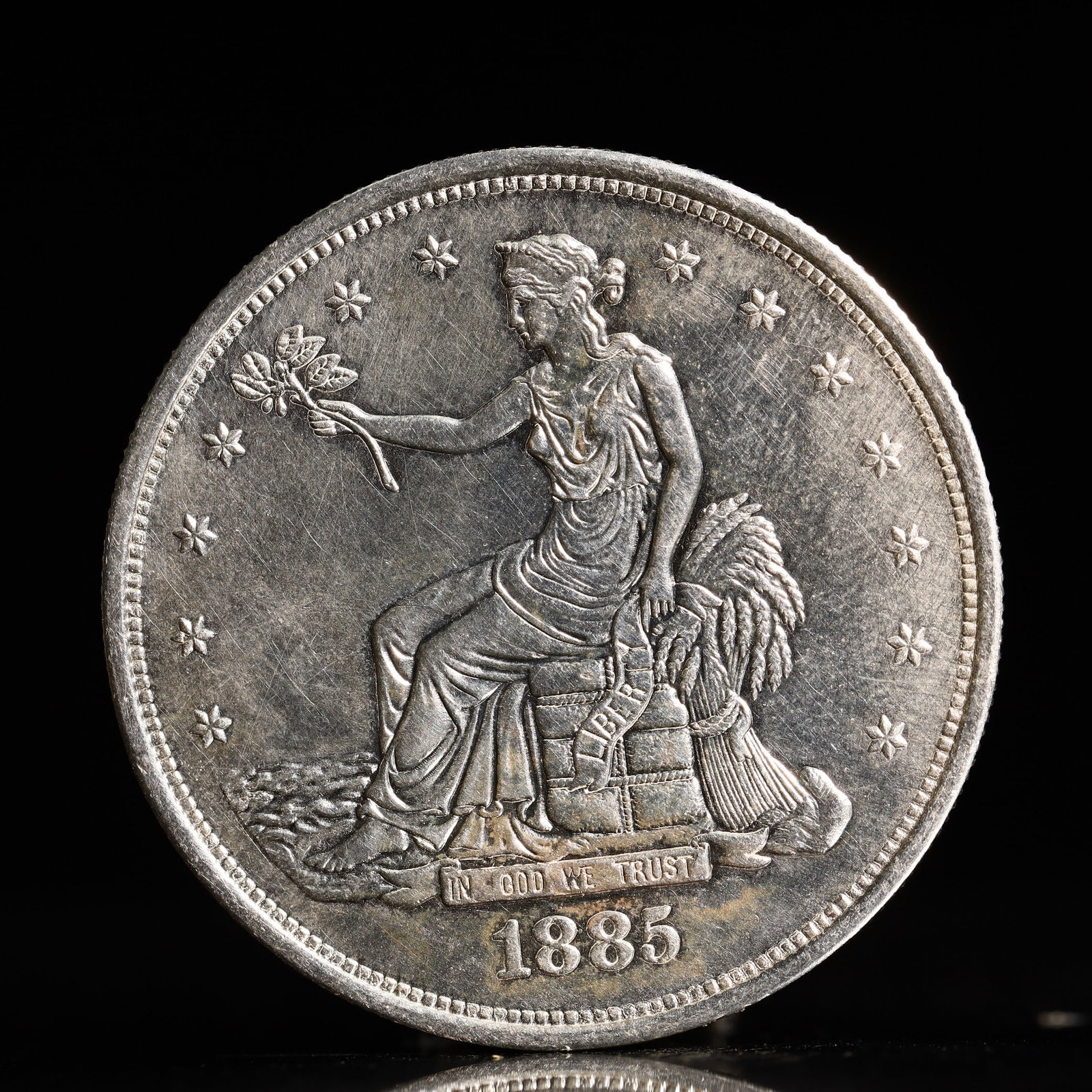 USA Trade Dollar 1885 Coin: American coin. Obverse: Liberty seated on a pedestal facing the sea to the left holding olive branches surrounded by 13 stars. IN GOD WE TRUST / LIBERTY / 1885. Reverse: An eagle holding branches with