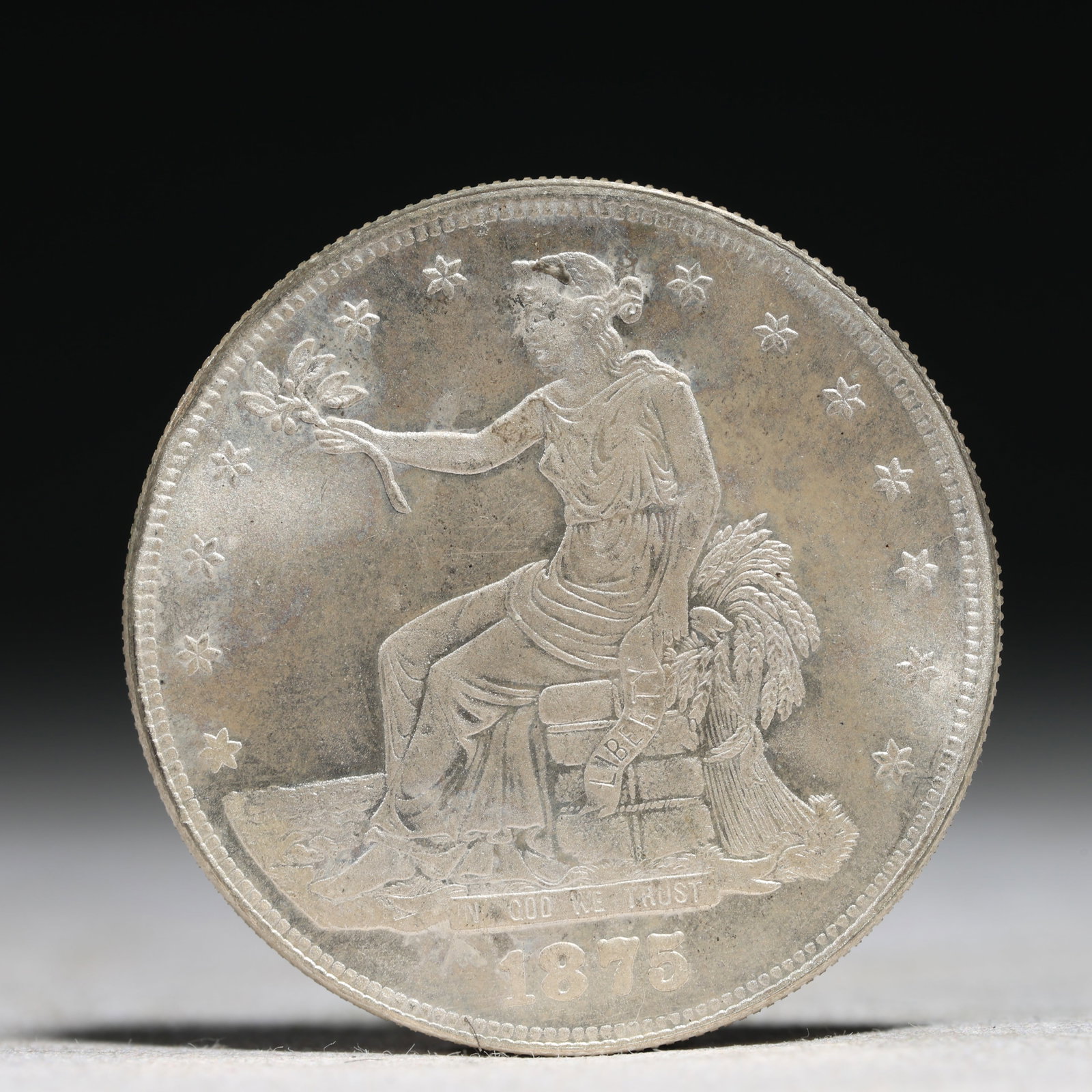 USA Trade Dollar 1875 Coin: American coin. Obverse: Liberty seated on a pedestal facing the sea to the left holding olive branches surrounded by 13 stars. IN GOD WE TRUST / LIBERTY / 1875. Reverse: An eagle holding branches with