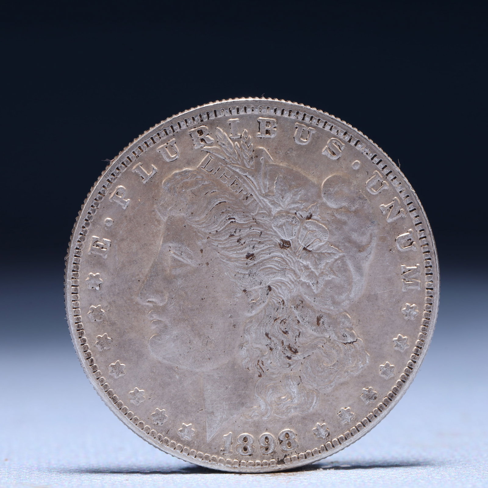 USA Morgan Dollar 1898 Coin: Obv: profile bust with date below and E PLURIBUS UNUM legend and stars around. Rev: eagle with In God we trust above within wreath with UNITED STATES OF AMERICA ONE DOLLAR legend. IN GOD WE TRUST / LI