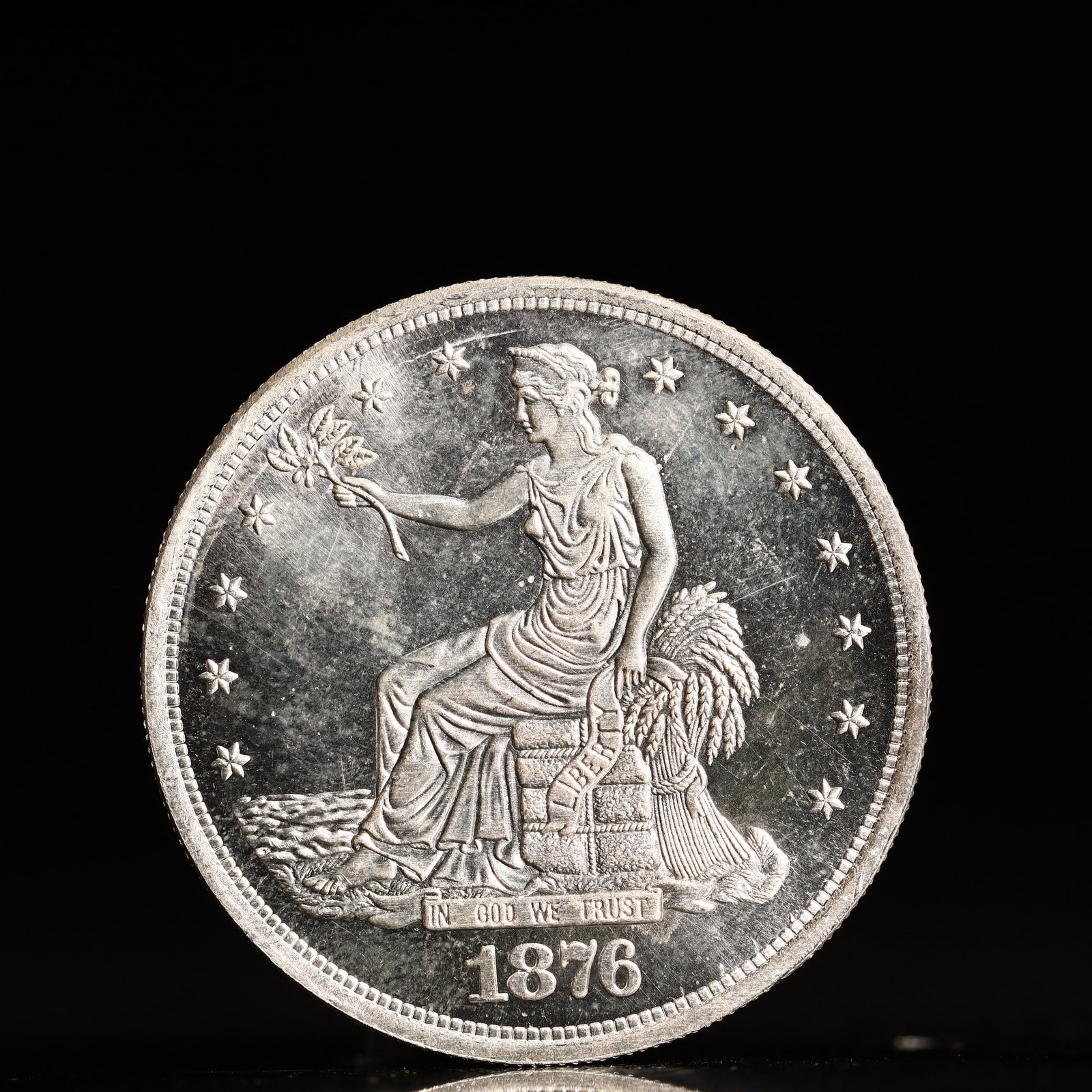 USA Trade Dollar 1876 Coin: American coin. Obverse: Liberty seated on a pedestal facing the sea to the left holding olive branches surrounded by 13 stars. IN GOD WE TRUST / LIBERTY / 1876. Reverse: An eagle holding branches with