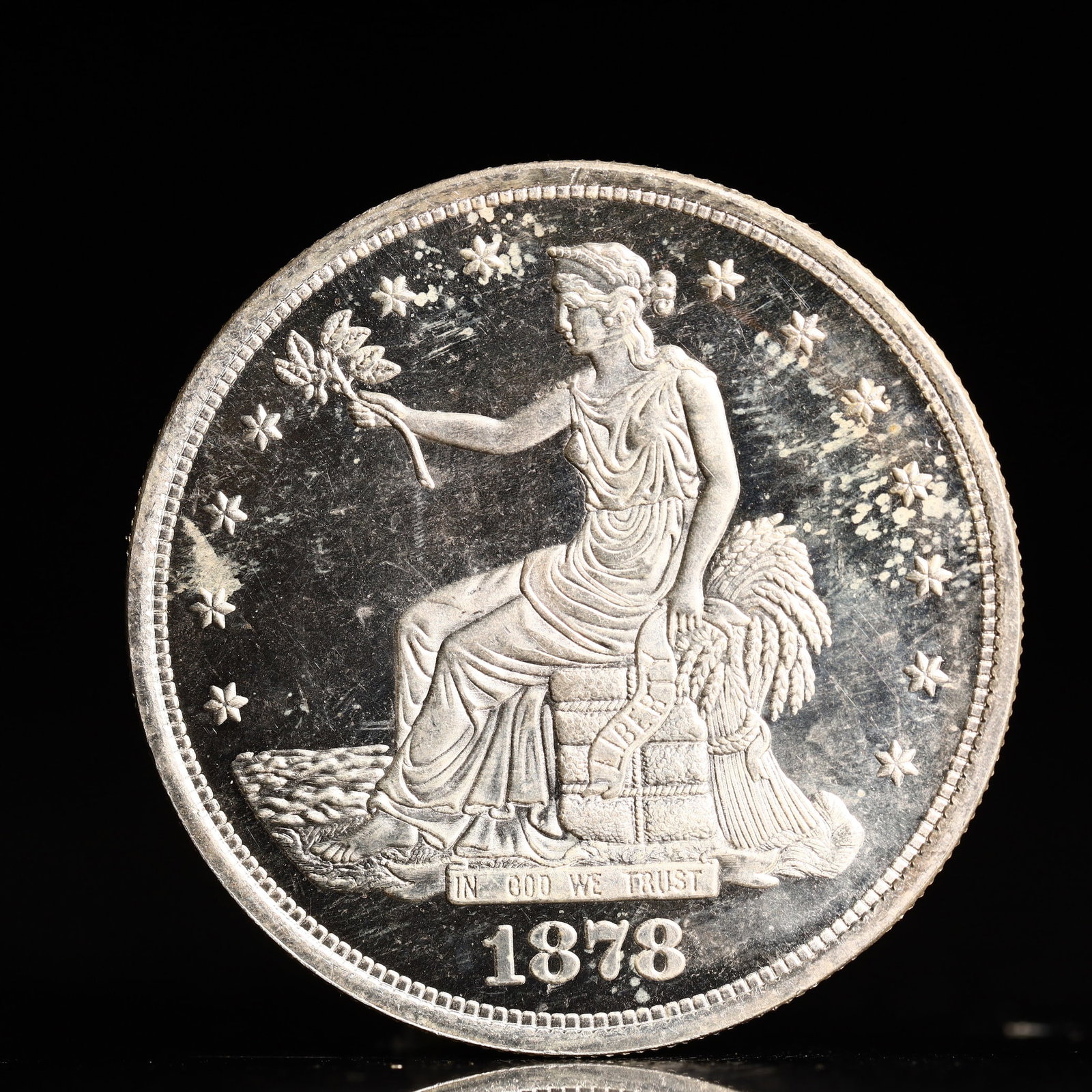 USA Trade Dollar 1878 Coin: American coin. Obverse: Liberty seated on a pedestal facing the sea to the left holding olive branches surrounded by 13 stars. IN GOD WE TRUST / LIBERTY / 1878. Reverse: An eagle holding branches with