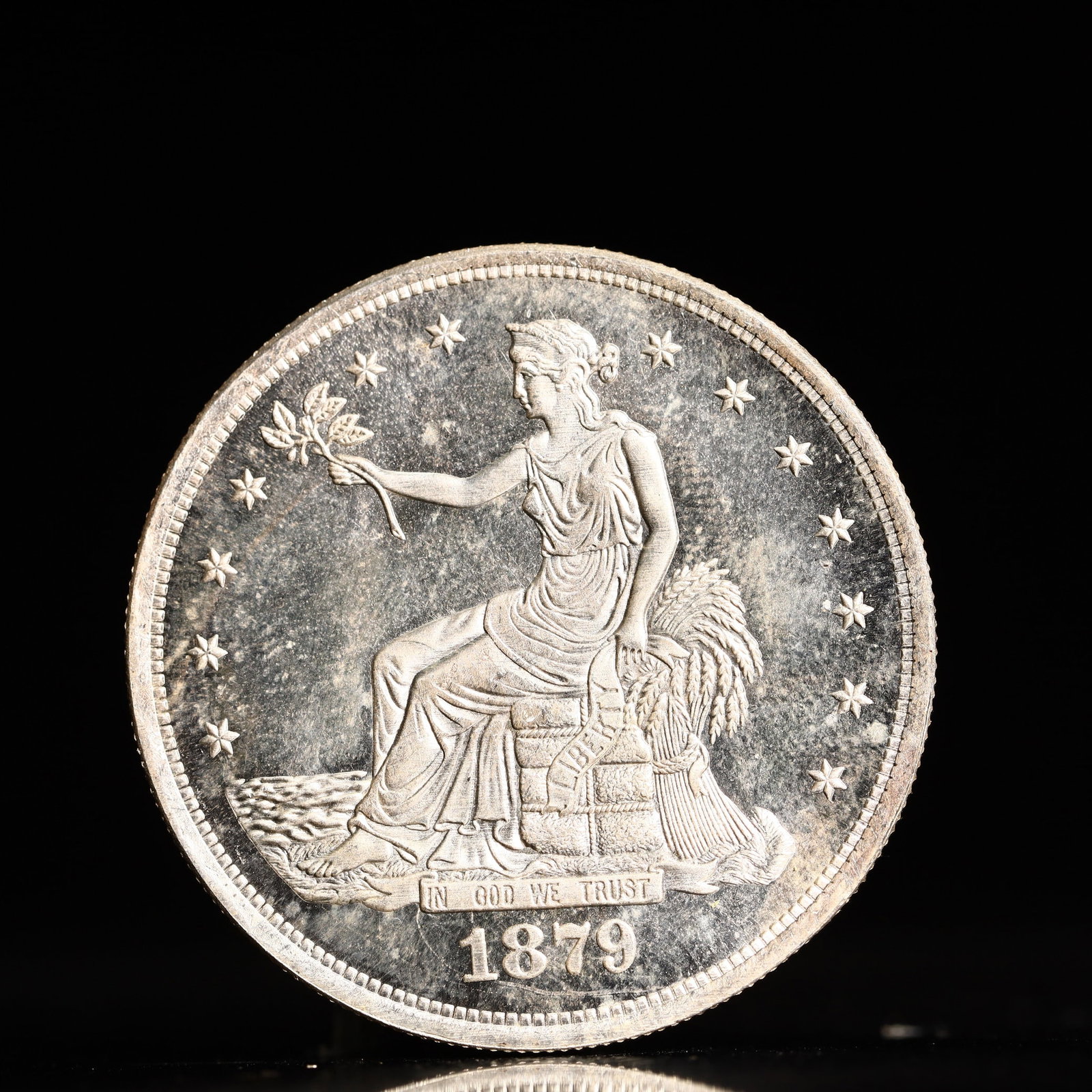USA Trade Dollar 1879 Coin: American coin. Obverse: Liberty seated on a pedestal facing the sea to the left holding olive branches surrounded by 13 stars. IN GOD WE TRUST / LIBERTY / 1879. Reverse: An eagle holding branches