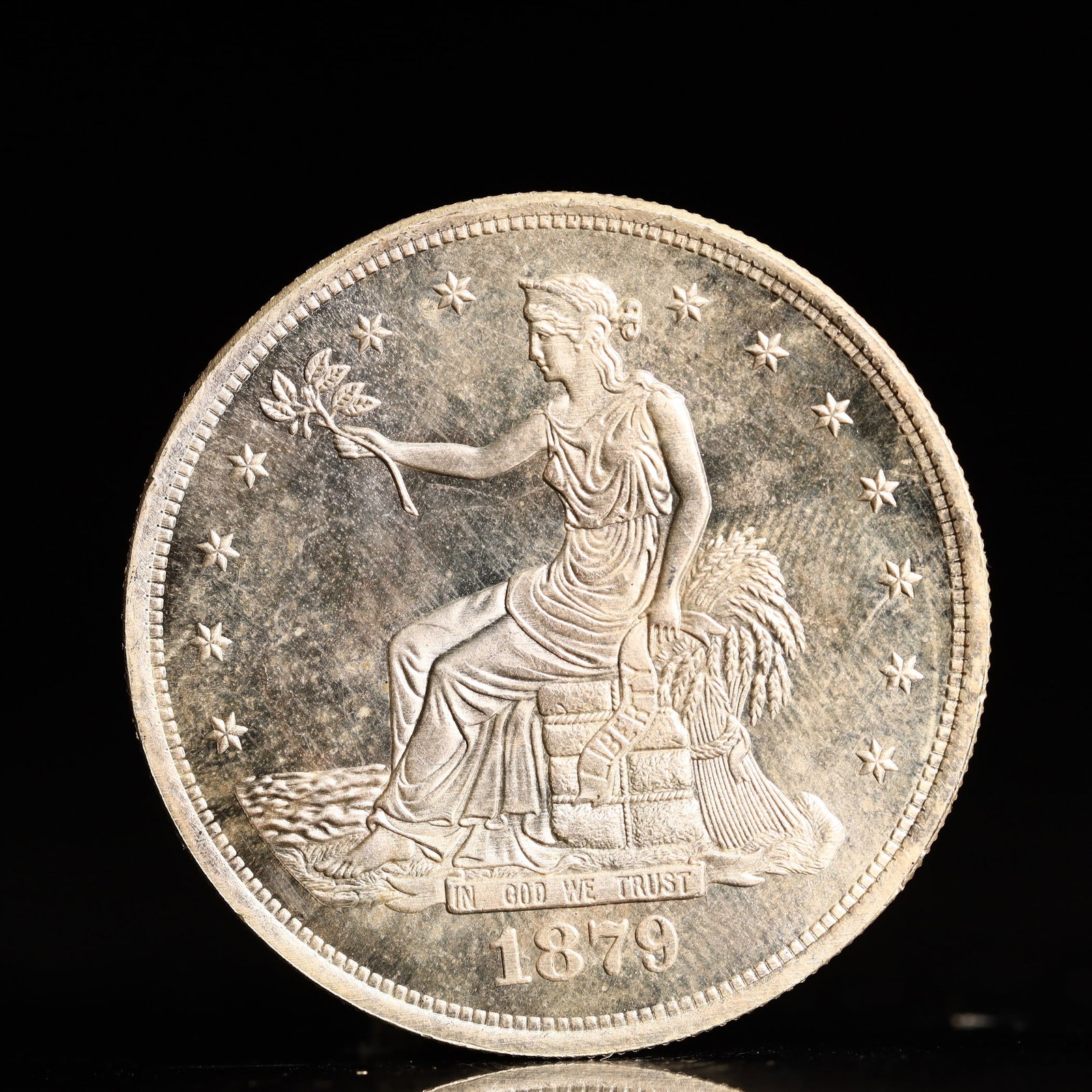 USA Trade Dollar 1879 Coin: American coin. Obverse: Liberty seated on a pedestal facing the sea to the left holding olive branches surrounded by 13 stars. IN GOD WE TRUST / LIBERTY / 1879. Reverse: An eagle holding branches with