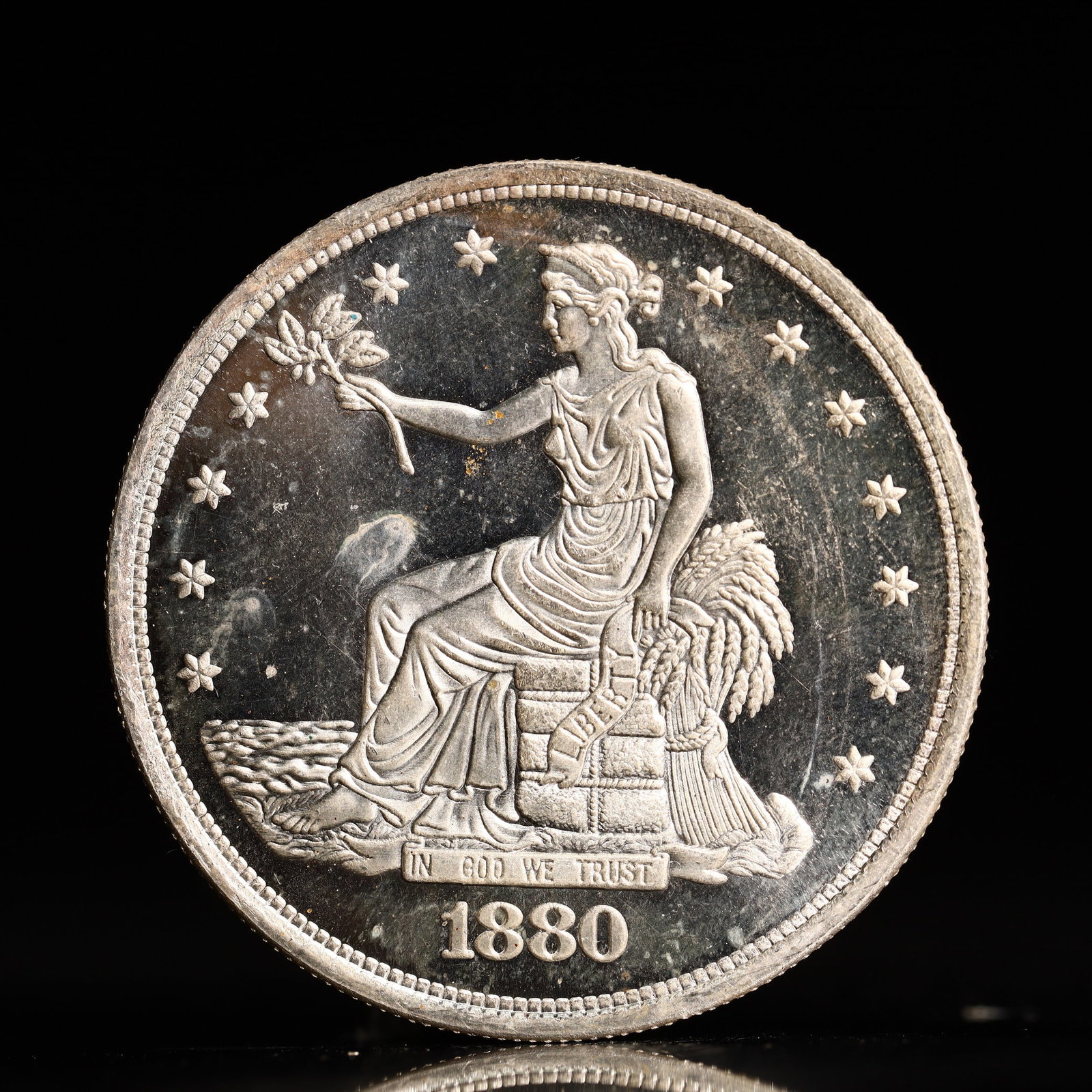 USA Trade Dollar 1880 Coin: American coin. Obverse: Liberty seated on a pedestal facing the sea to the left holding olive branches surrounded by 13 stars. IN GOD WE TRUST / LIBERTY / 1880. Reverse: An eagle holding branches with