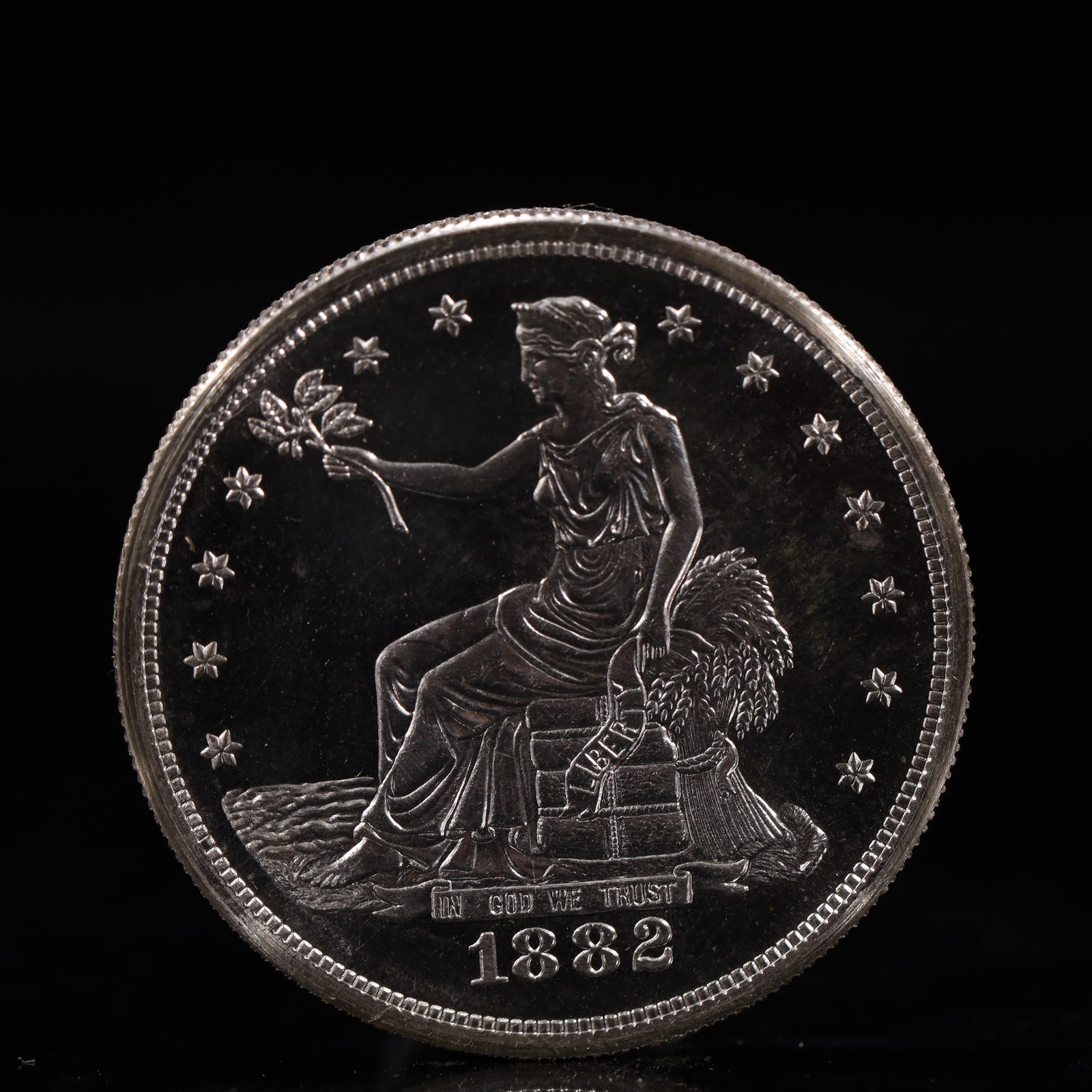 USA Trade Dollar 1882 Coin: American coin. Obverse: Liberty seated on a pedestal facing the sea to the left holding olive branches surrounded by 13 stars. IN GOD WE TRUST / LIBERTY / 1882. Reverse: An eagle holding branches with