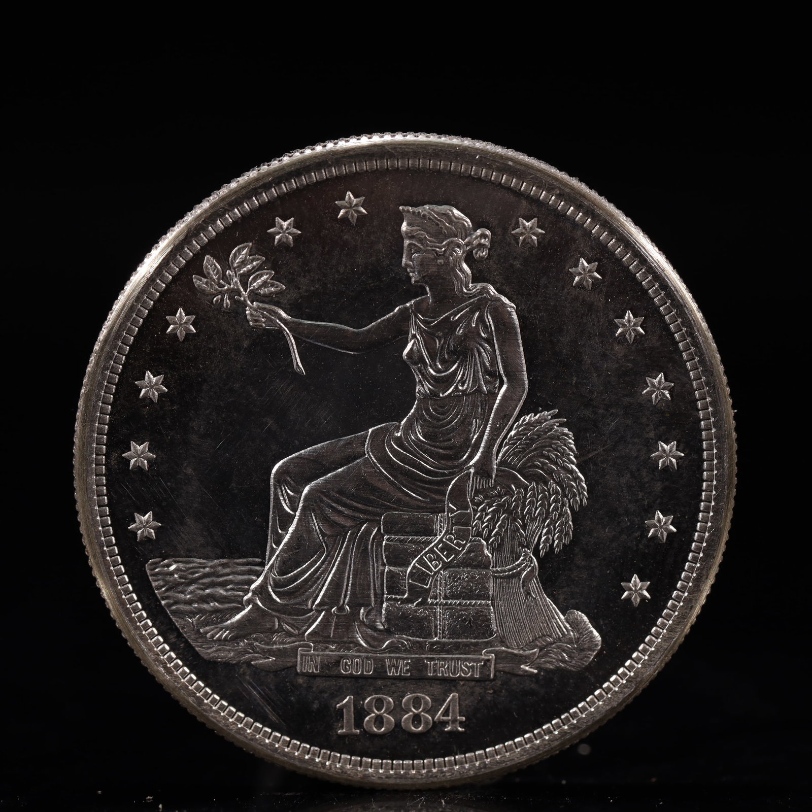 USA Trade Dollar 1884 Coin: American coin. Obverse: Liberty seated on a pedestal facing the sea to the left holding olive branches surrounded by 13 stars. IN GOD WE TRUST / LIBERTY / 1884. Reverse: An eagle holding branches