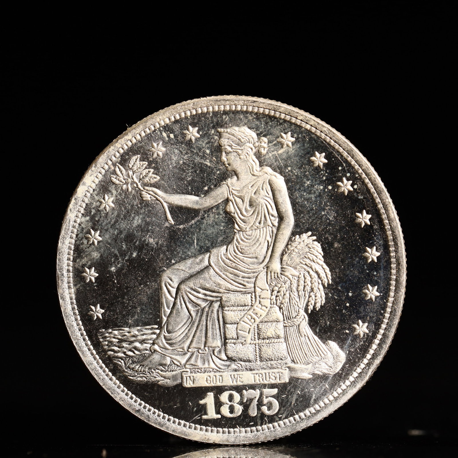 USA Trade Dollar 1875 Coin: American coin. Obverse: Liberty seated on a pedestal facing the sea to the left holding olive branches surrounded by 13 stars. IN GOD WE TRUST / LIBERTY / 1875. Reverse: An eagle holding branches with