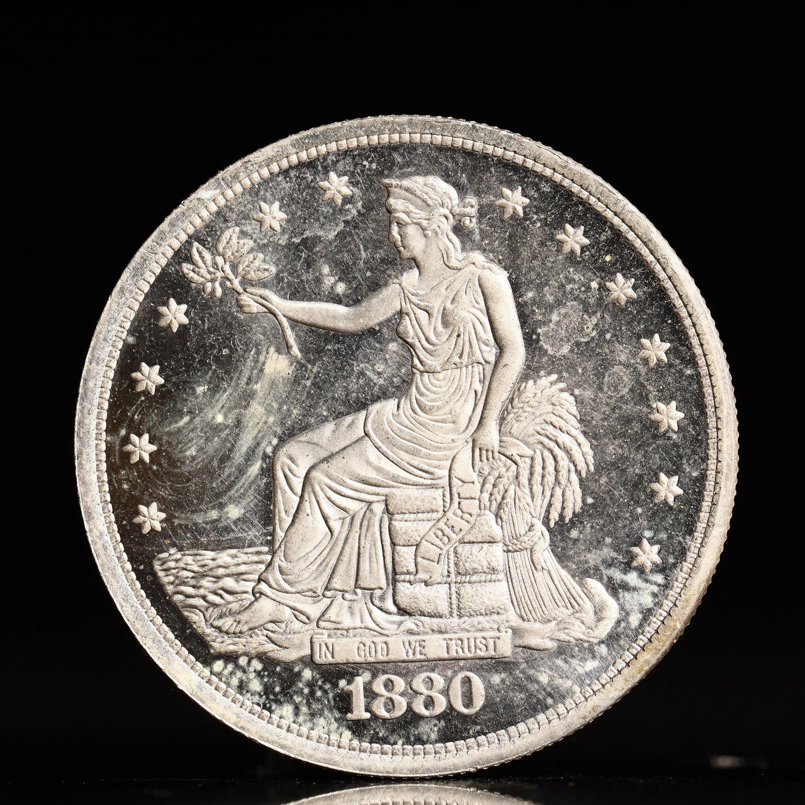USA Trade Dollar 1880 Coin: American coin. Obverse: Liberty seated on a pedestal facing the sea to the left holding olive branches surrounded by 13 stars. IN GOD WE TRUST / LIBERTY / 1880. Reverse: An eagle holding branches with