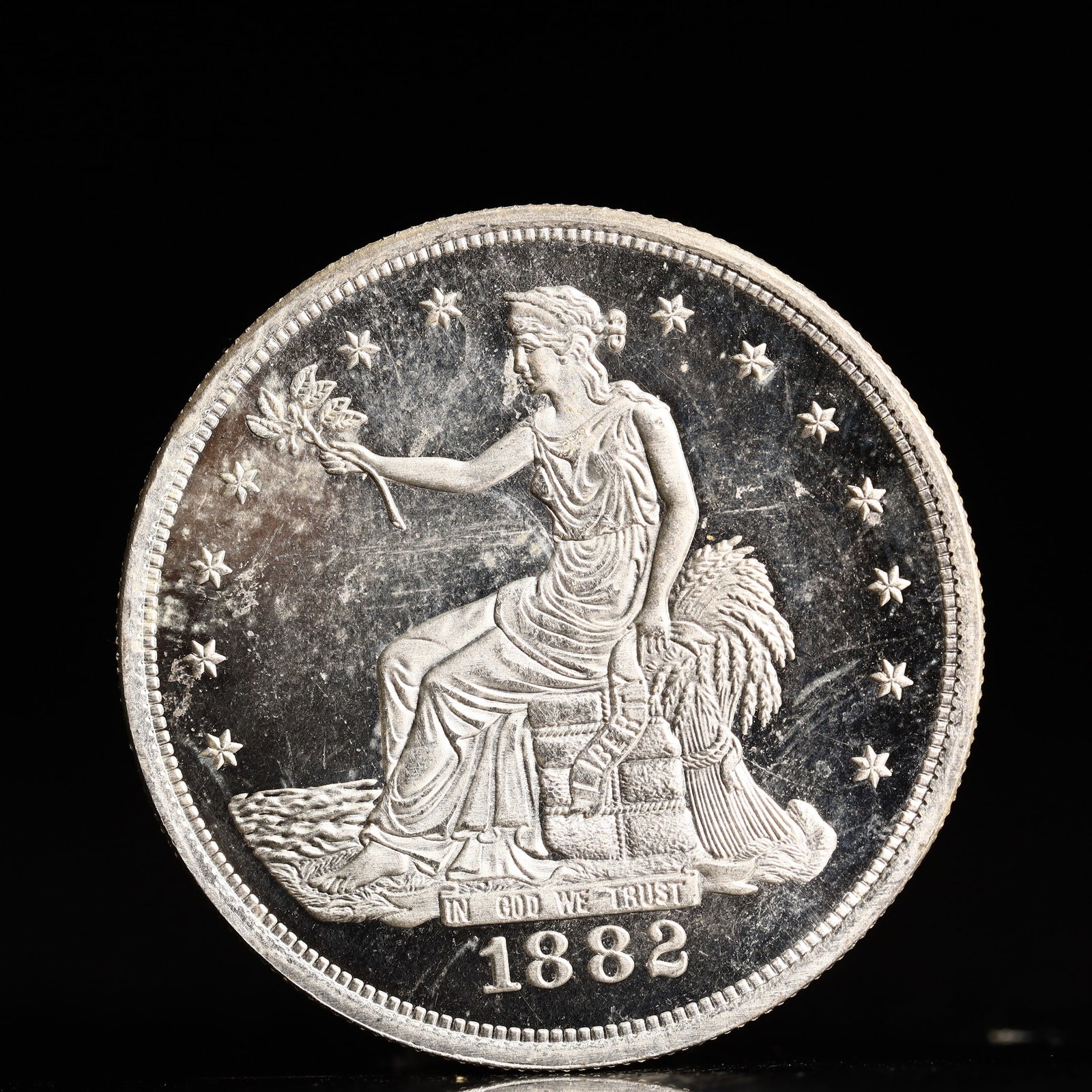 USA Trade Dollar 1882 Coin: American coin. Obverse: Liberty seated on a pedestal facing the sea to the left holding olive branches surrounded by 13 stars. IN GOD WE TRUST / LIBERTY / 1882. Reverse: An eagle holding branches with