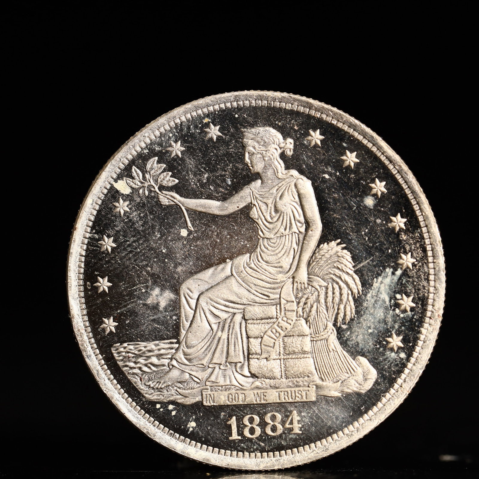 USA Trade Dollar 1884 Coin: American coin. Obverse: Liberty seated on a pedestal facing the sea to the left holding olive branches surrounded by 13 stars. IN GOD WE TRUST / LIBERTY / 1884. Reverse: An eagle holding branches
