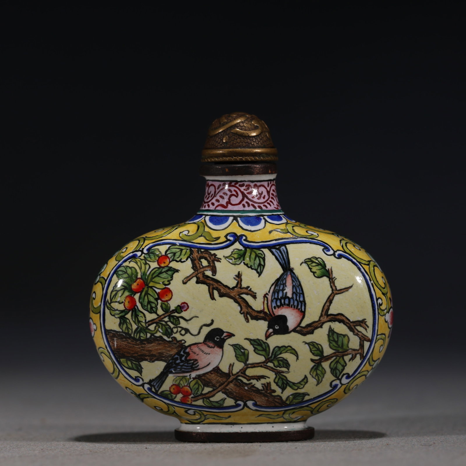 A Chinese Painted Enamel Snuff Bottle with Birds and Flowers,Qianlong Mark: A Chinese yellow-ground painted enamel snuff bottle,decorated with two birds perched on a branch with clusters of grapes.Fitted with a bronze stopper.The base bears a four-character mark reading(Qianl