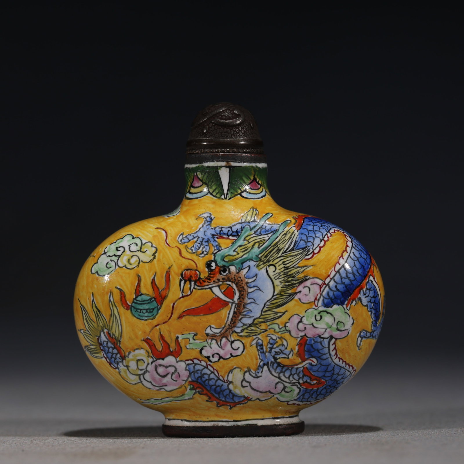 A Chinese Painted Enamel Snuff Bottle with Dragon and Phoenix,Qianlong Mark: A Chinese yellow-ground painted enamel snuff bottle,decorated with a blue dragon chasing a flaming pearl on one side and a phoenix in flight on the other,amidst clouds.Fitted with a bronze stopper.The