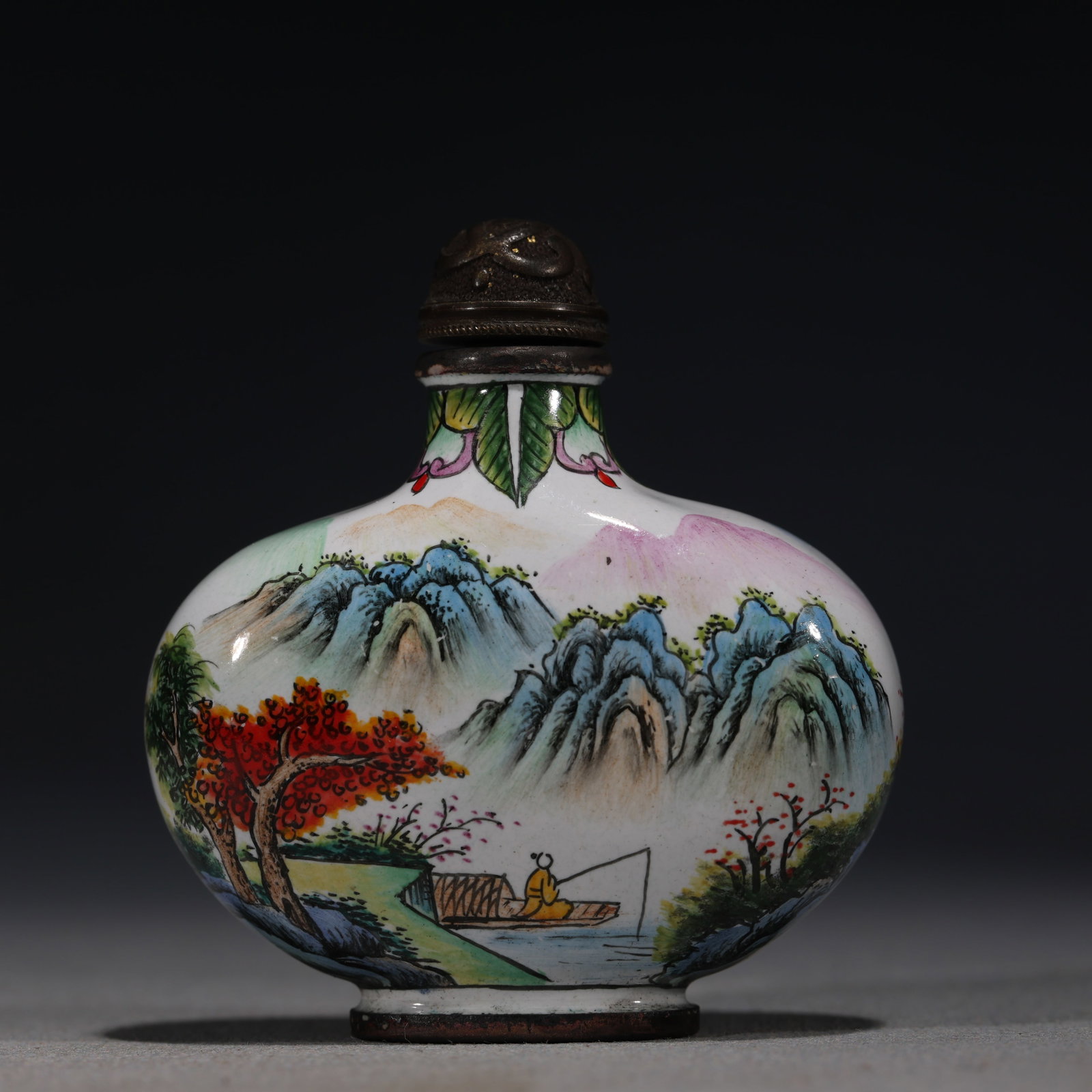 A Chinese Painted Enamel Snuff Bottle with Landscape,Qianlong Mark: A Chinese painted enamel snuff bottle,finely decorated with a continuous landscape featuring mountains,trees,and a fisherman in a boat.Fitted with a bronze stopper.The base bears a four-character mark