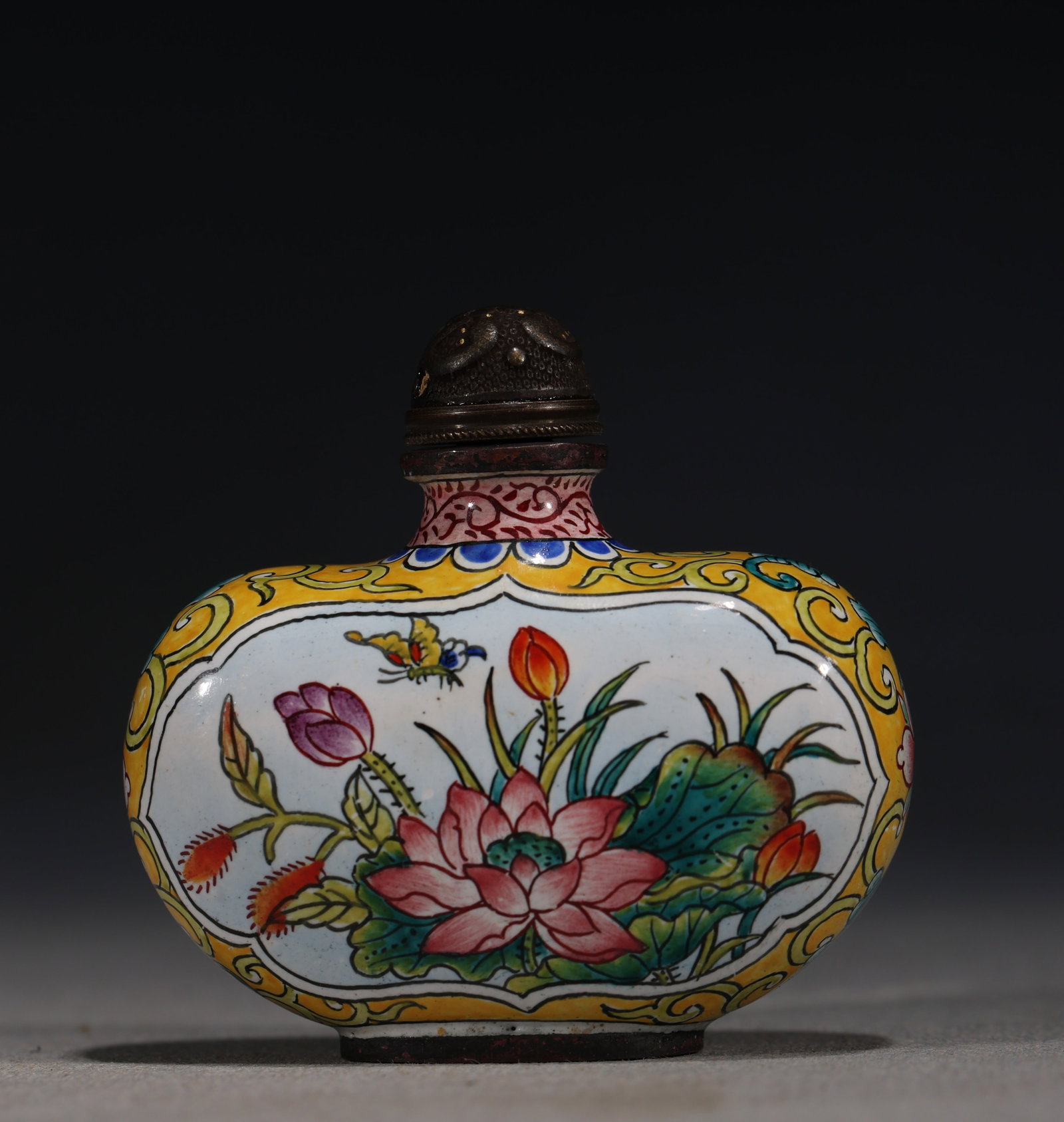 A Chinese Canton Enamel Snuff Bottle with Lotus and Dragonfly,Qianlong Mark: A Chinese painted enamel snuff bottle,decorated with a lotus pond scene featuring a dragonfly and butterfly amidst blooming lotus.Fitted with a bronze stopper.The base bears a four-character mark