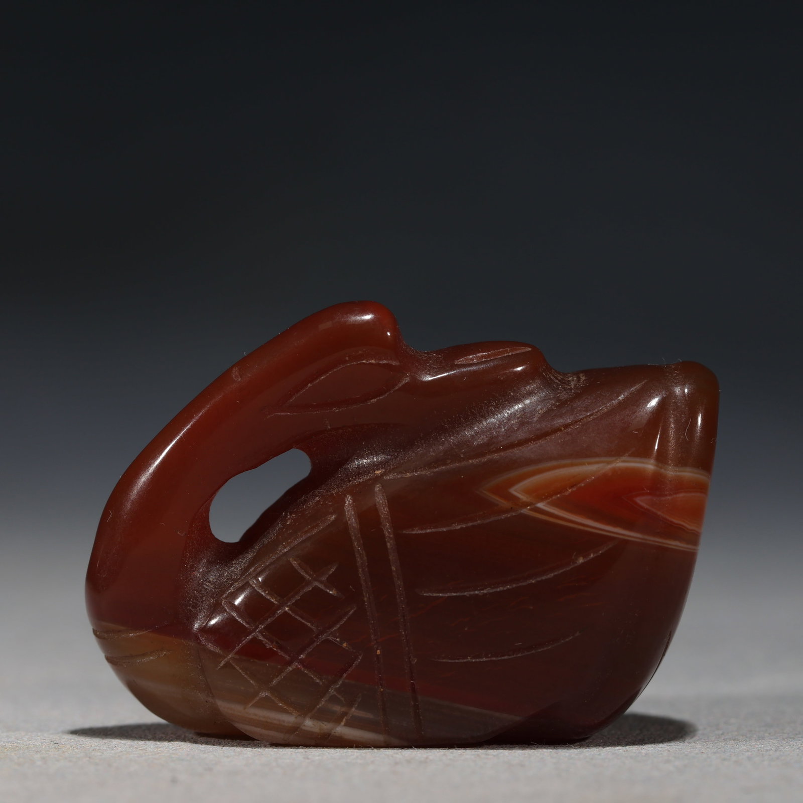 RED AGATE CARVED DUCK PENDANT: A distinctive red agate ornament carved in the shape of a duck or waterfowl,featuring curved lines representing wings,a crosshatch pattern on the body,and a loop at the top for suspension. Dated 