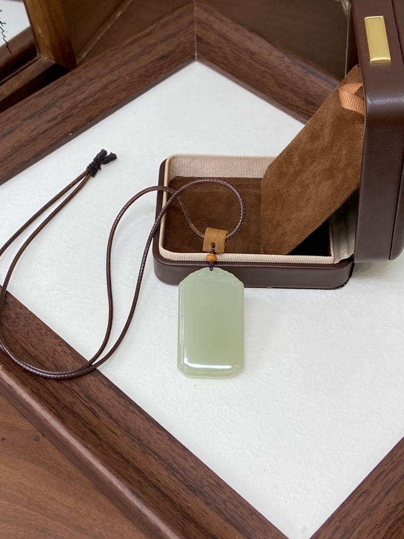 A Chinese Vertical Scroll Ink Painting of Flower on Paper: A finely polished Hetian jade pendant of rectangular form, of icy translucency and even 'qingshui' (clear water) tone, left plain as a 'Ping An' plaque symbolizing peace and protection. The jade is of
