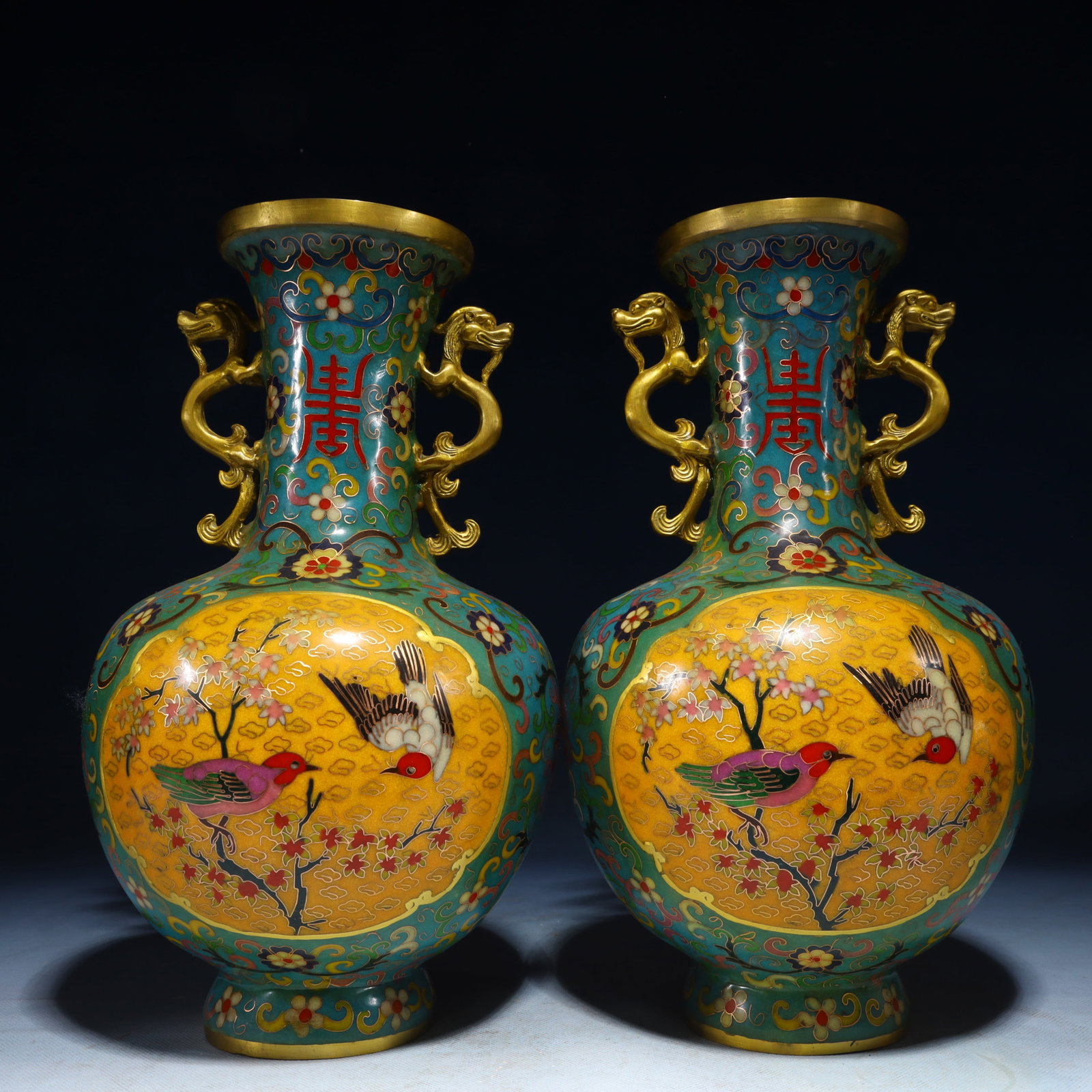 An Exquisite Gilt Bronze Lotus Pattern Ornament: A matching pair of cloisonné enamel vases decorated with birds perched among flowering branches, the shoulders set with double handles, each with a four-character Qianlong mark. 一对&