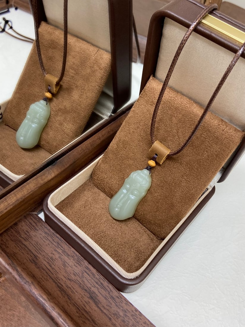 A Hongshan Culture Agate 'Dragon' Pendant: A Hetian jade pendant of Xinjiang Youqing (oily green) material, carved as a Buddha with an elongated face and large ears, a traditional iconography of good fortune. The jade is of fine, oily texture 