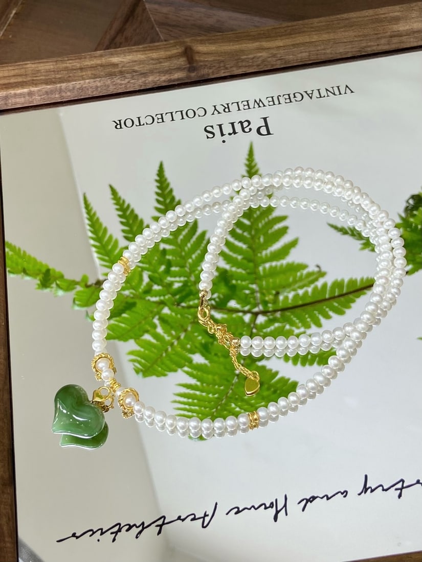 A Solemn Gilt Bronze Statue of Amitayus,Inlaid Turquoise: A finely carved Hetian jade pendant of spinach-green tone, carved as a pitaya, set in 18K gold and suspended from a strand of natural freshwater pearls. The pendant measures 19.7mm by 17mm by 10.6mm. 