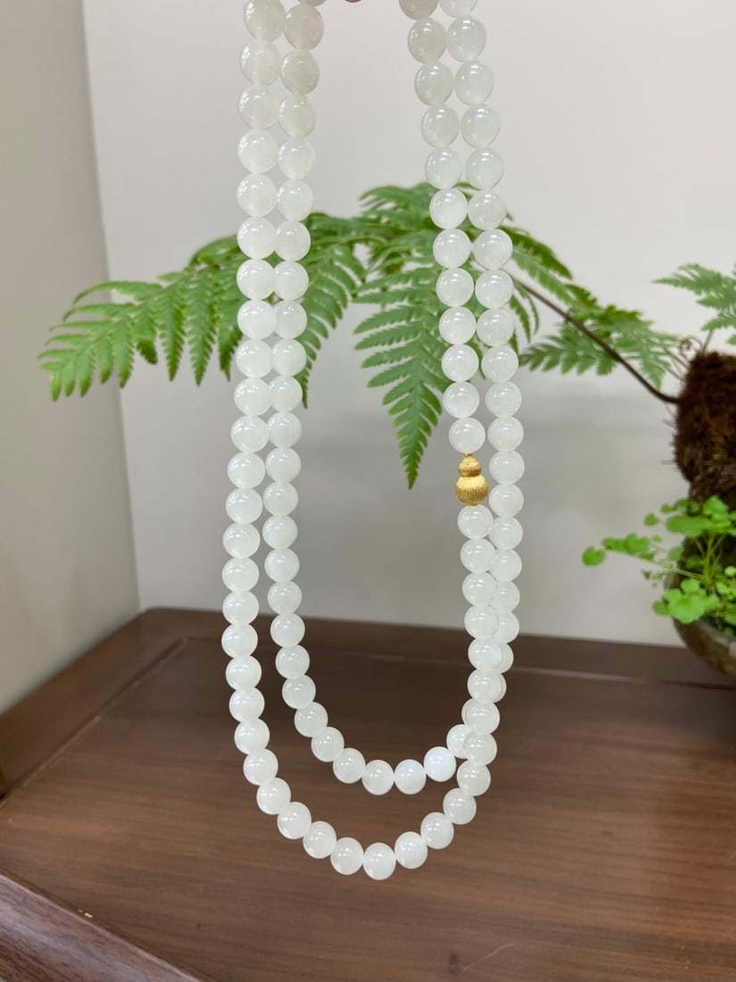 An Exquisite Eaglewood Figure Ornament: A finely carved Hetian jade necklace of 'noubo' (glutinous-icy) white quality, composed of 108 round beads of 8mm diameter. The jade is of fine, even quality with a cool, elegant presence. The necklac