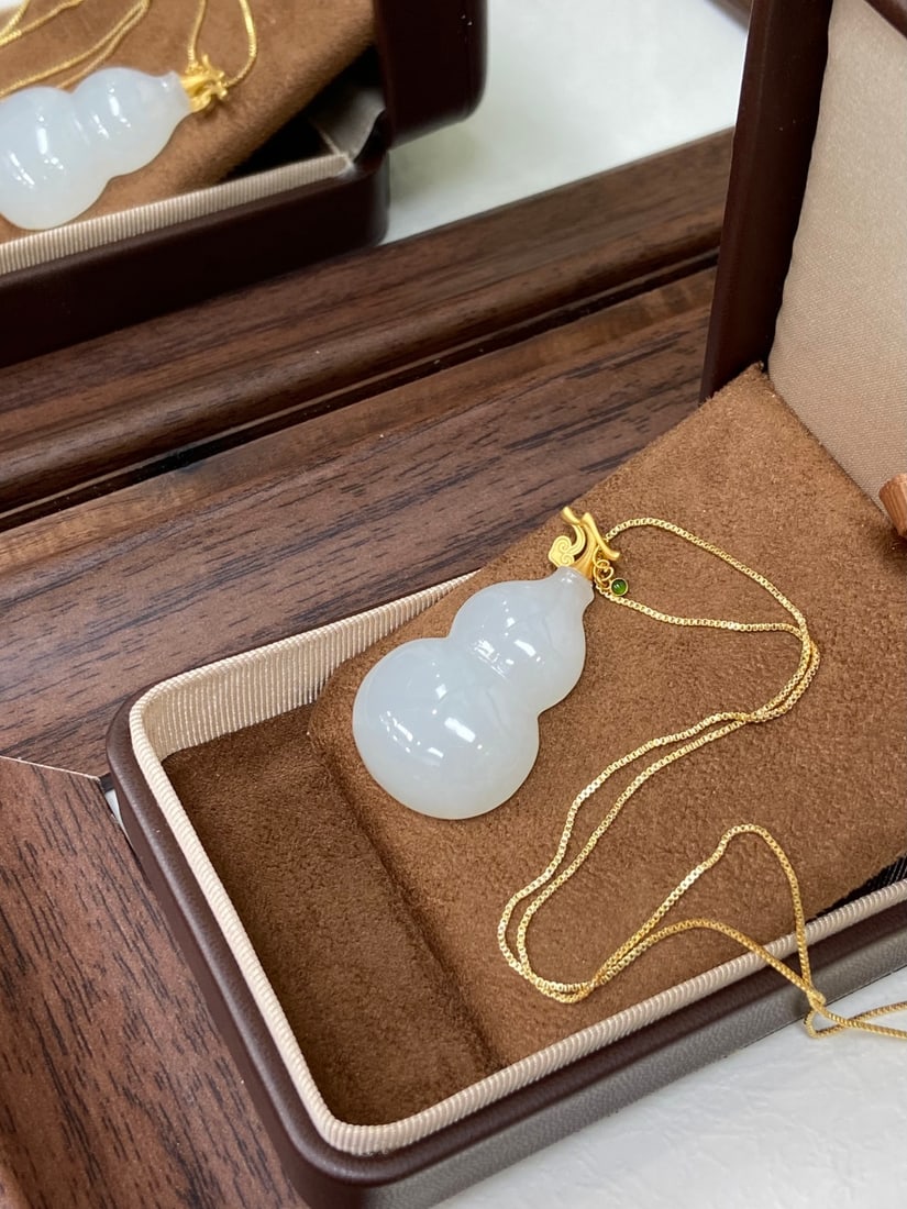 A Finely Carved Hetian Jade White Jade Gourd Pendant: A finely carved Hetian jade pendant of white tone, set in 18K gold, carved as a gourd, a symbol of blessing and prosperity. The jade is of fine, icy texture with a smooth, luminous finish. The pendant