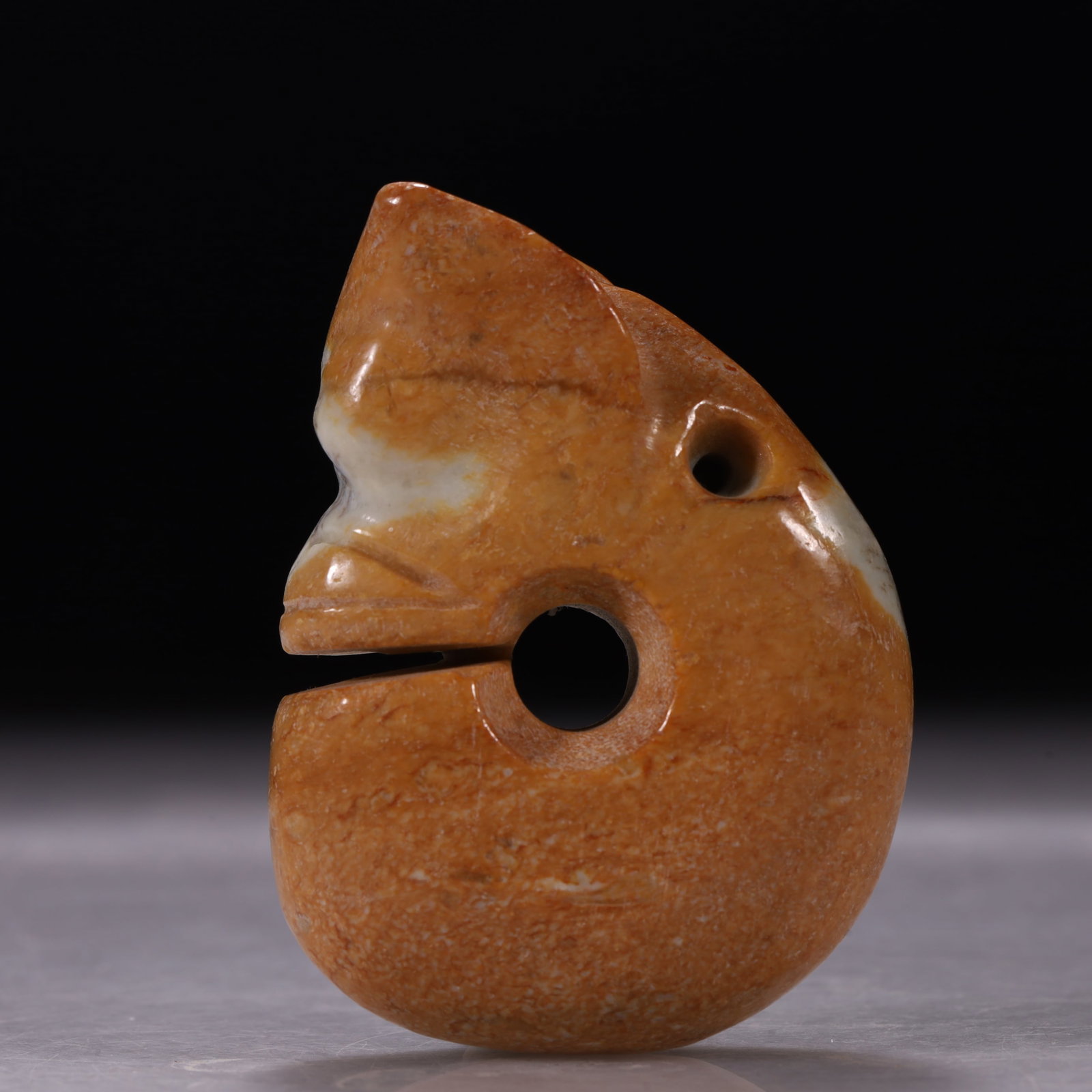 Hongshan Culture Grey-Yellow Jade Pig-Dragon With Dark Inclusions: Coiled pig-dragon, plump and rounded, featuring a large central hole. The eyes are carved as large circular rings using low-relief techniques. The jade is grey-yellow with distinct dark brown/black in