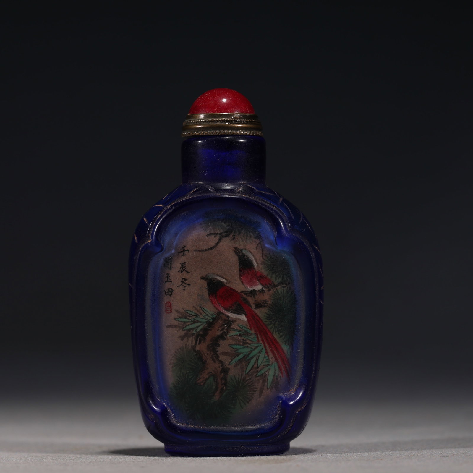 A Chinese Inside-Painted Blue Overlay Glass Snuff Bottle with Birds on Pine,Renchen Year: An inside-painted blue overlay glass snuff bottle,painted with a pair of birds on a pine branch.Inscribed Renchen Dong.Fitted with a red stopper.The base is unmarked.Size:1.6inx0.7inx2.9in,清