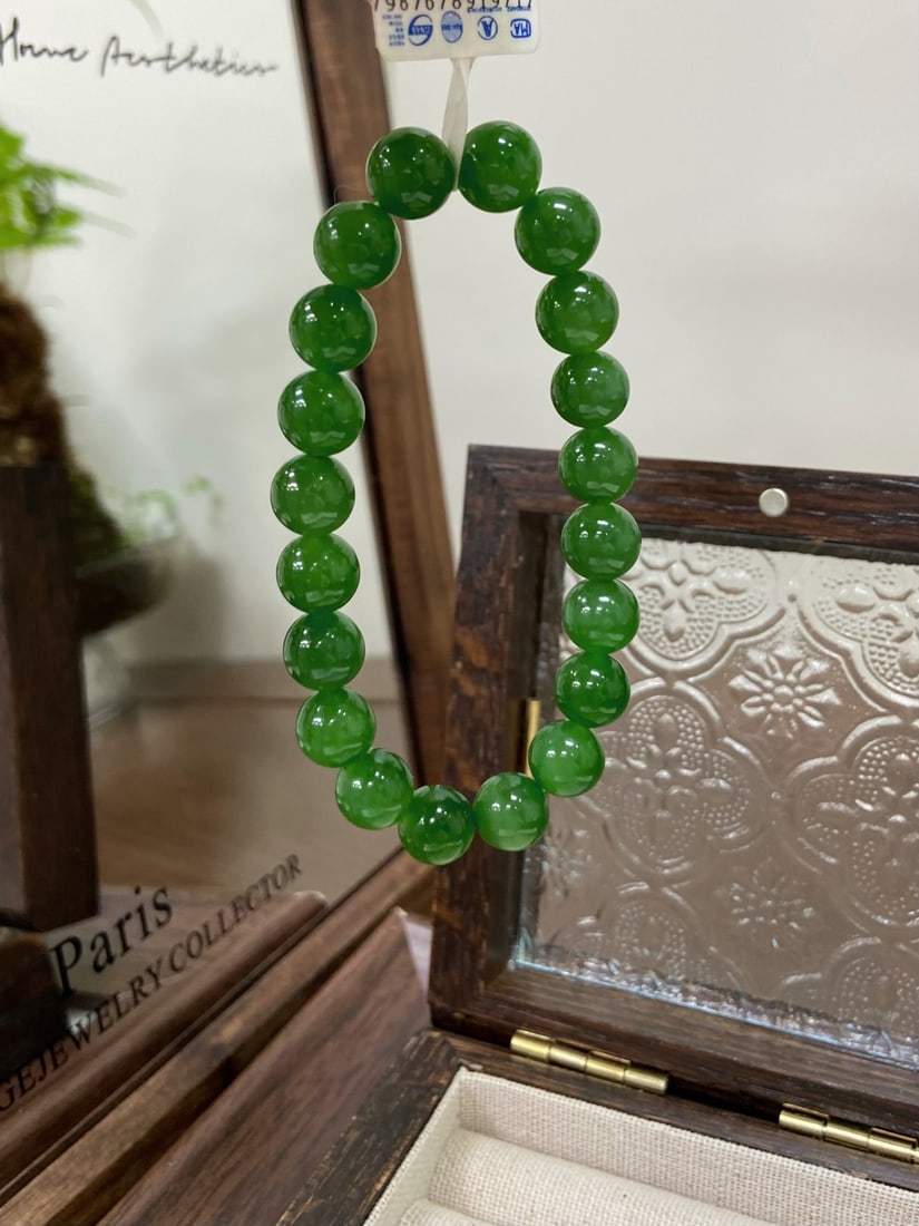 A Finely Carved Hetian Jade 'Ice Yang Green' Spinach-Green Bracelet: A finely carved Hetian jade bracelet of 'ice yang green' spinach-green quality, composed of round beads of 10mm diameter. The jade is of fine, icy texture with a vibrant, fresh green hue, free of mine