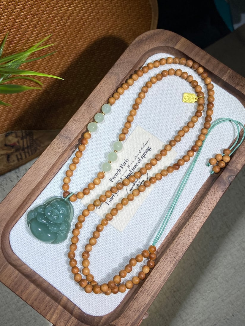 A Finely Carved Hetian Jade 'Fenqing' 'Maitreya Buddha' Pendant: A finely carved Hetian jade pendant of 'fenqing' (powder-green) quality, carved as a seated Maitreya Buddha, accompanied by a wooden bead chain. The jade is of fine, icy texture with a smooth, luminou