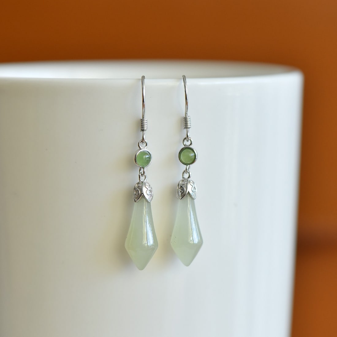 A Pair of Sterling Silver and White Jade Magnolia Drop Earrings: A pair of sterling silver drop earrings, each set with a white jade magnolia, Sise: 7mm×16 mm. 纯银镶白玉玉兰花耳坠；主