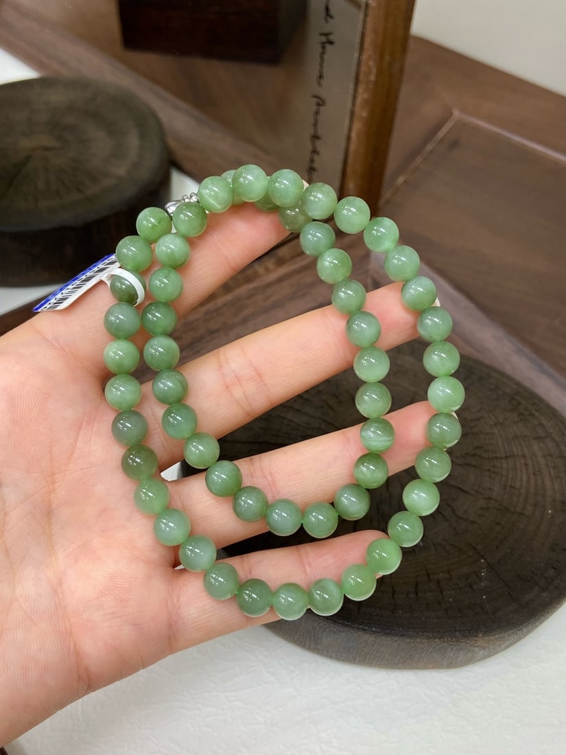 A Finely Carved Hetian Jade Spinach-Green 'Cat's Eye' Necklace: A finely carved Hetian jade necklace of spinach-green quality, composed of round beads of 8mm diameter, exhibiting a cat's-eye effect. The jade is of fine, icy texture with a smooth, luminous finish. 