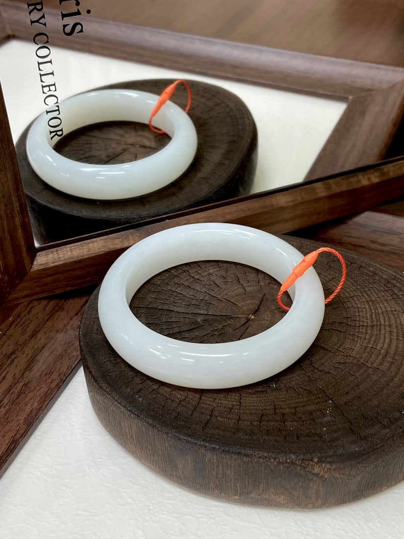 A Finely Carved Hetian Jade 'Yangzhi' White Jade Bangle: A finely carved Hetian jade bangle of 'yangzhi' (mutton-fat) white quality, of round form. The jade is of fine, oily texture with a warm, glutinous finish. The bangle measures 56mm in circumference